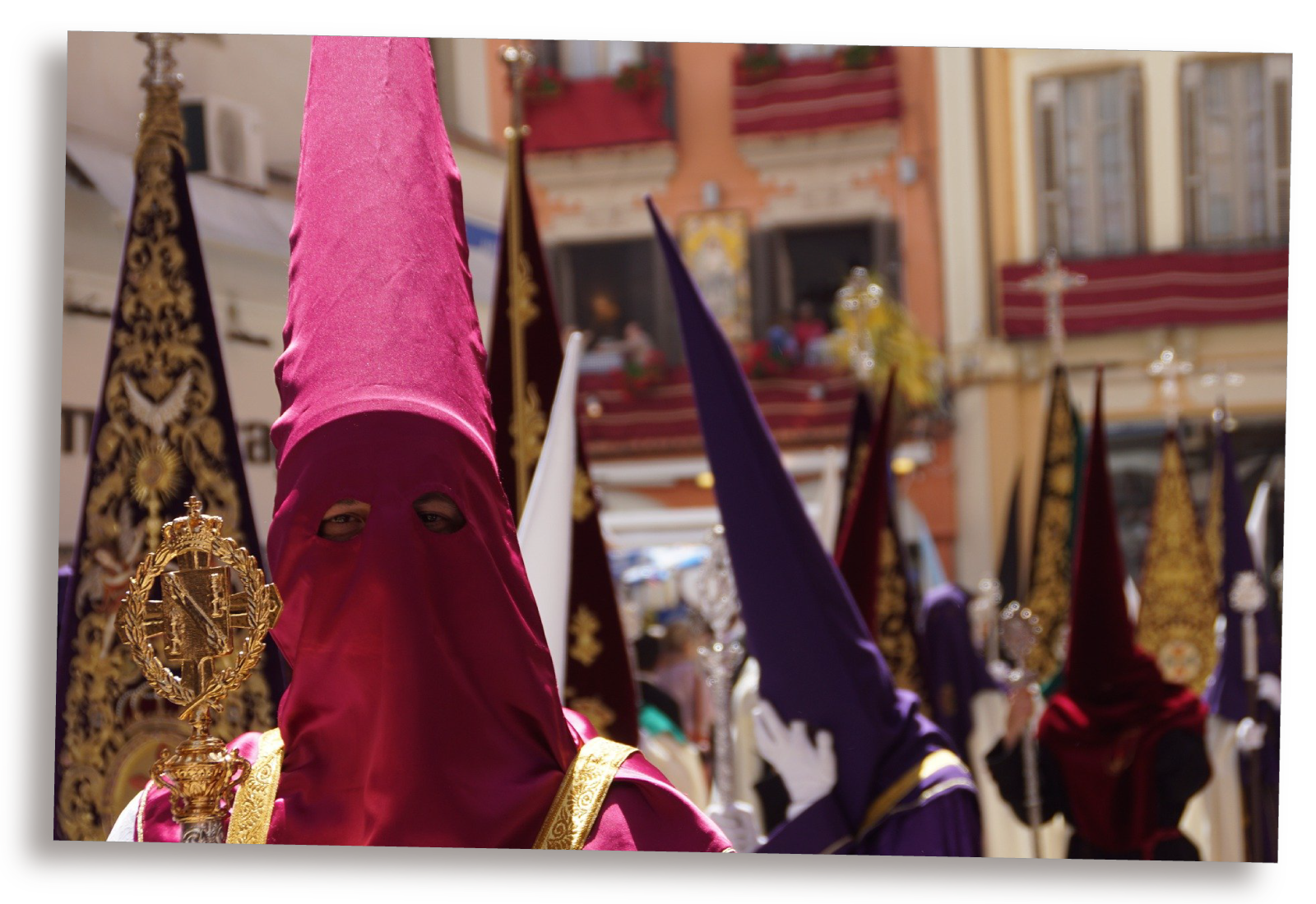 Ilustracja przedstawia procesję składającą się z osób w kolorowych spiczastych kapturach, z wyciętymi dziurami jedynie na oczy.