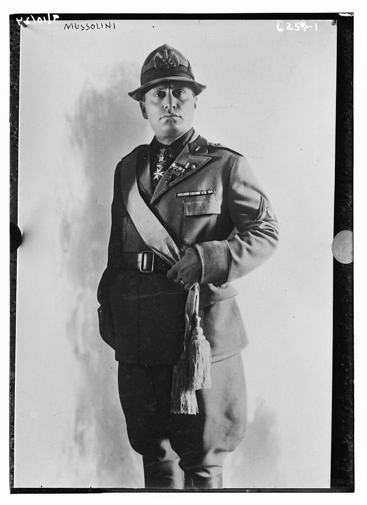 Zdjęcie przedstawia młodego mężczyznę w mundurze z bufiastymi nogawkami wpuszczonymi w wysokie buty. Marynarkę munduru ma spiętą w pasie szerokim pasem. przez ramię ma przewieszoną szarfę. Na szyi ma medal w kształcie krzyża maltańskiego. Na głowie ma kapelusz z małym rondem i orłem z przodu.