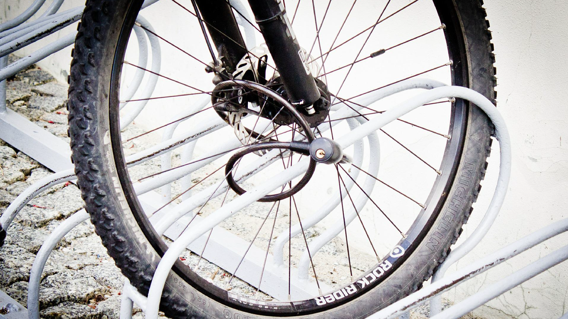 Zdjęcie przedstawia koło roweru przypięte linką zabezpieczającą do stojaka.