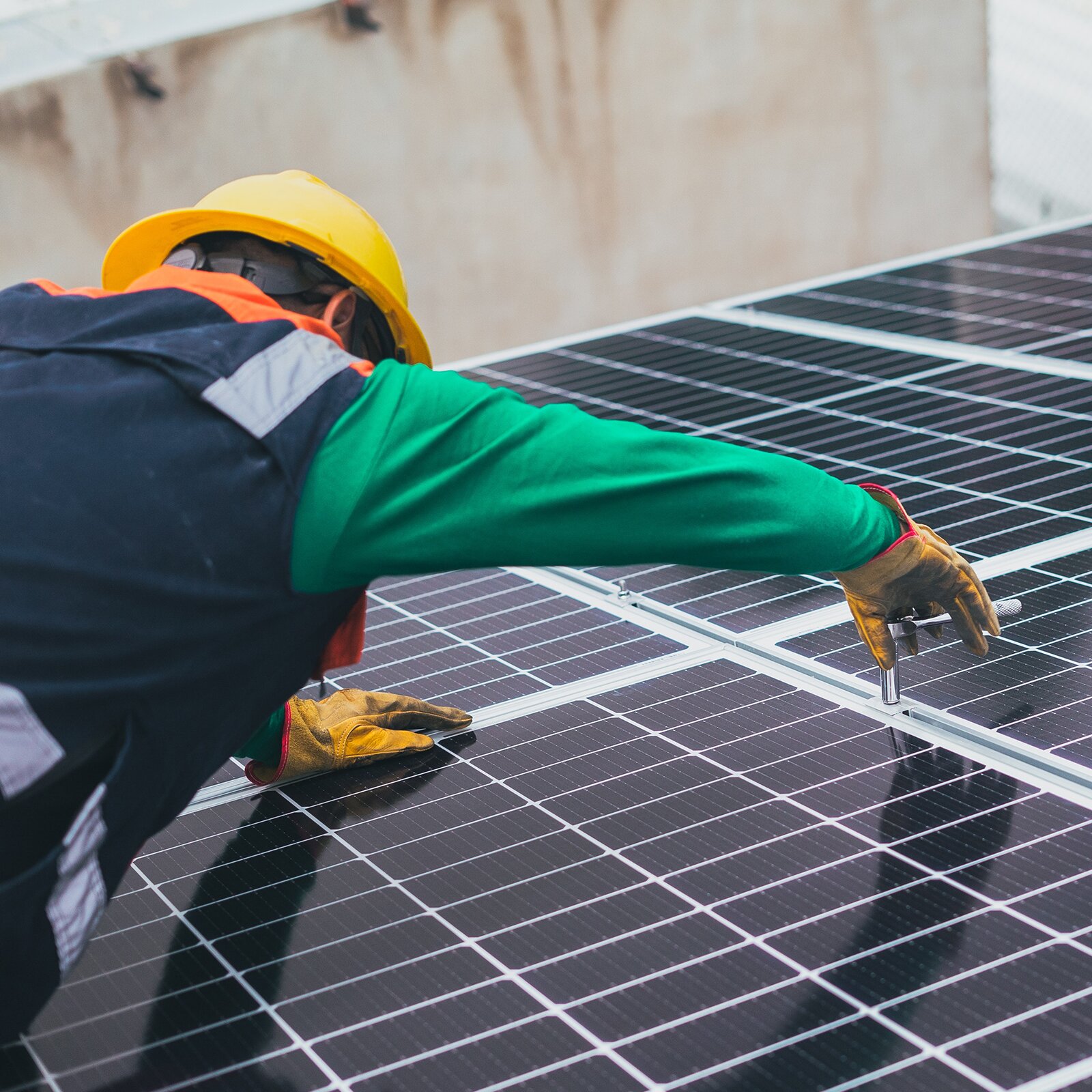 Na zdjęciu widoczny jest mężczyzna w kasku montujący panele fotowoltaiczne.