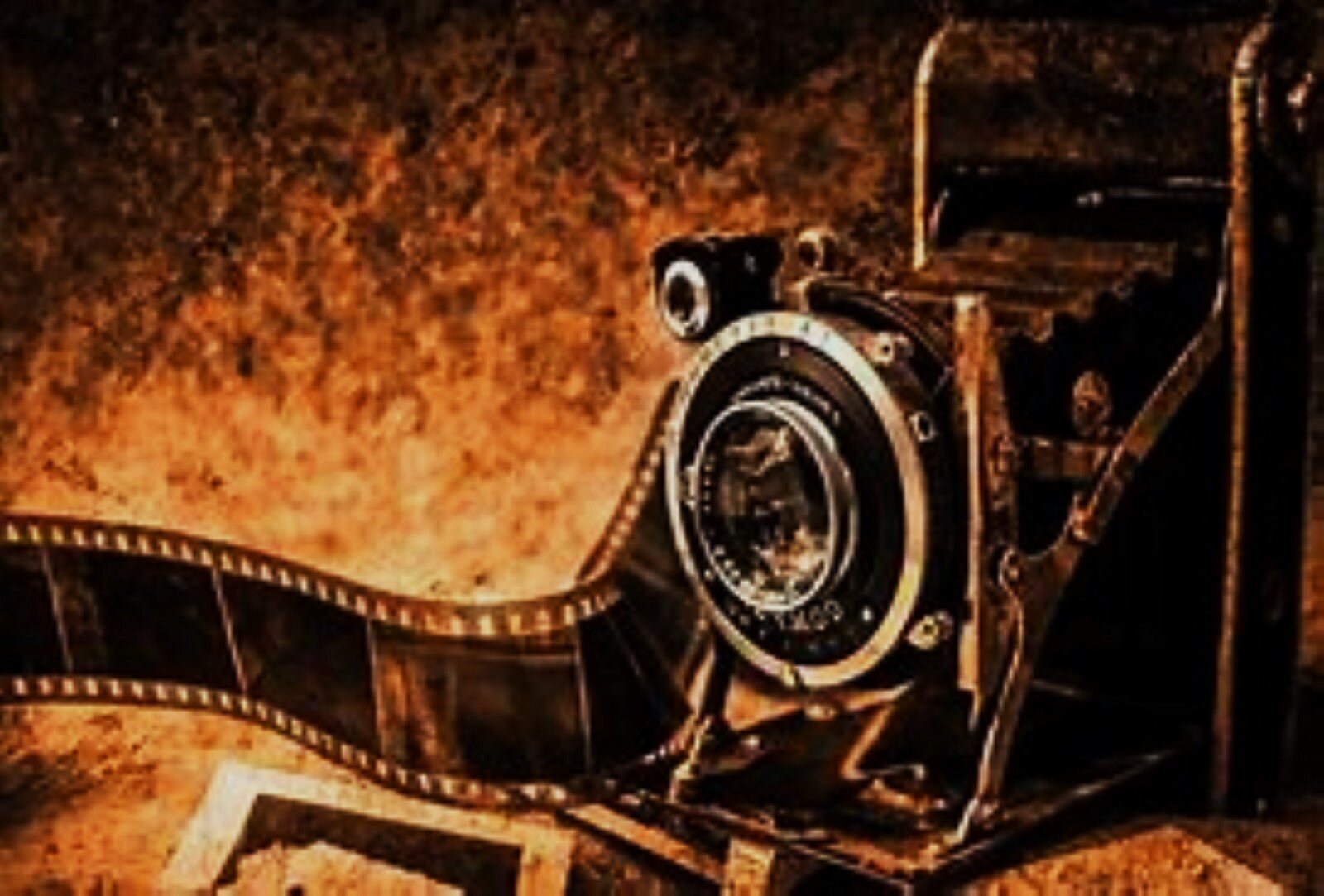 Zdjęcie przedstawia stary model aparatu fotograficznego i wijącą się obok kliszę fotograficzną. Za nimi fakturowa powierzchnia ściany.