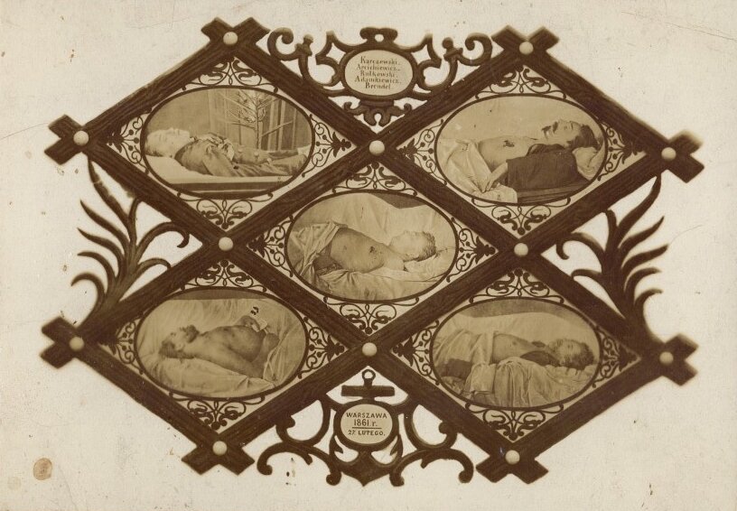 Ilustracja przedstawia pięć zdjęć, które umieszczone zostały w osobnych, okrągłych ramkach. Wszystkie pięć ramek składa się na ozdobny, drewniany stojak na zdjęcia. Na fotografiach widnieje pięciu nieżywych mężczyzn spoczywających na łózkach, w białej pościeli. Widać ich głowy oraz w przypadku czterech z nich nagie torsy, poniżej których ciała okryte są pościelą. Na klatkach piersiowych widać rany od postrzałów. Jedno zdjęcie przedstawia zwłoki mężczyzny ubranego w mundur. 