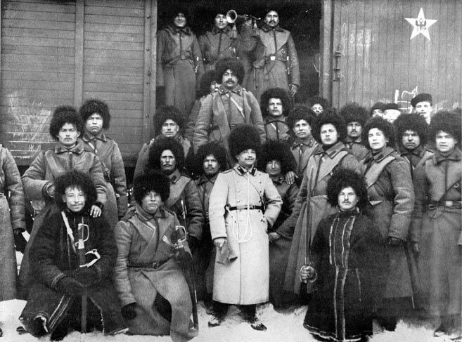 Fotografia przedstawia grupę rosyjskich żołnierzy pozujących na tle otwartego wagonu pociągu towarowego. Cześć mężczyzn stoi w wagonie, pozostali ustawieni są przed nim. Wszyscy ubrani są w długie płaszcze zimowe oraz duże, futrzane czapy. W centralnym punkcie,  stoi uśmiechający się mężczyzna w wojskowym, jasnym płaszczu dwurzędowym z naramiennikami oraz wysokiej, futrzanej czapce. Klęczący obok niego żołnierze uzbrojeni są w szable. 