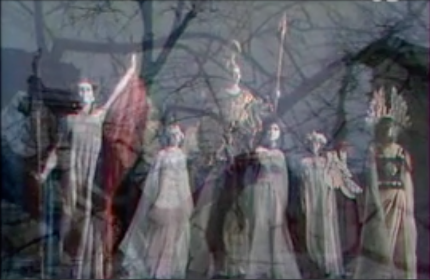 Fotografia przedstawia nakładające się na siebie dwa obrazy. Ukazane są tutaj stojące postaci. Są wyprostowane, unoszą głowy. Część postaci ubrana jest w obszerne, długie szaty. Pośrodku stoi umundurowana kobieta. Ma hełm na głowie. W lewej dłoni trzyma włócznię. W tle znajdują się bezlistne drzewa. Panuje mrok.