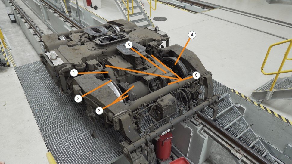 Zrzut ekranu przedstawia przykładową infografikę. Widoczne jest zdjęcie wózka napędnego ustawionego na torze w jasnym pomieszczeniu. Na grafice widać sześć punktów z liczbami, które po kliknięciu wyświetlają dodatkowe informacje o elementach przedstawionych na zdjęciu. W górnym lewym rogu widać przycisk z przekreślonym okiem służący do ukrywania punktów.