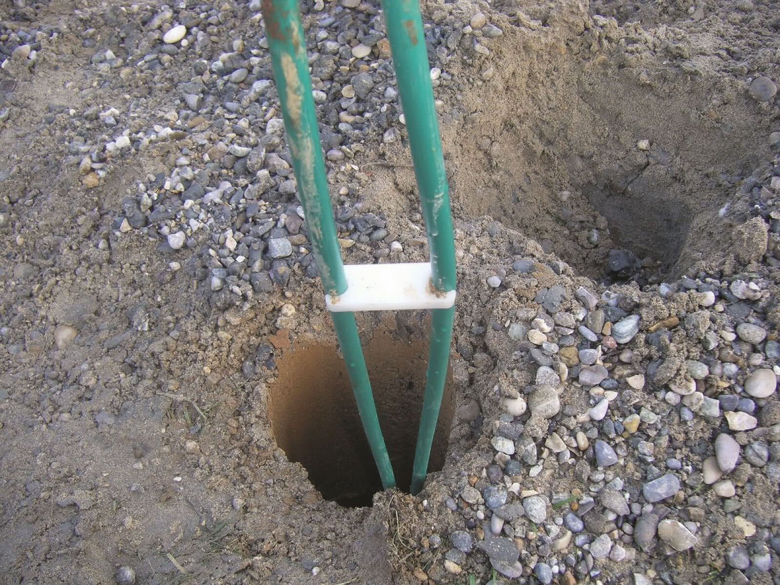 Na zdjęciu widoczny jest głęboki otwór w ziemi, do którego zostają wprowadzone dwa przewody sondy. Pomiędzy przewodami znajduje się sztywny element zapewniający dystans.