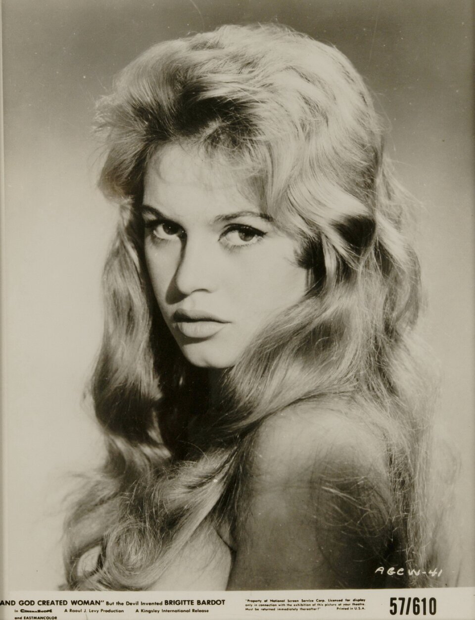Fotografia przedstawia plakat promujący film „I Bóg stworzył kobietę”. Na pierwszym planie obecna jest Brigitte Bardot - młoda, blondwłosa kobieta, spoglądająca w stronę obiektywu. Na jej oczach można zauważyć makijaż w postaci ciemnej kreski na górnej linii rzęs, jej skóra jest jasna, a usta lekko rozchylone. Kobieta ma krótką grzywkę, częściowo zaczesaną do tyłu, a średniej długości włosy przykrywają jej nagą skórę.  Pod wizerunkiem aktorki widoczny jest biały pasek, na którym zostały zawarte informacje o filmie.