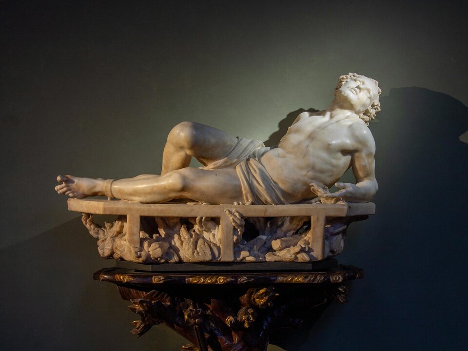 Ilustracja przedstawia marmurową rzeźbę „Świętego Wawrzyńca” Gianlorenza Berniniego. Na czarnym tle ukazuje młodego Wawrzyńca leżącego na ruszcie. Mężczyzna podpiera się na lewym ramieniu, lewą nogę ma wyprostowaną, prawą - lekko ugiętą w kolanie. Jego głowa jest odchylona. Delikatnie umięśnione ciało przewiązane jest na biodrach tkaniną. Pod rusztem widoczne jest płonące drewno.