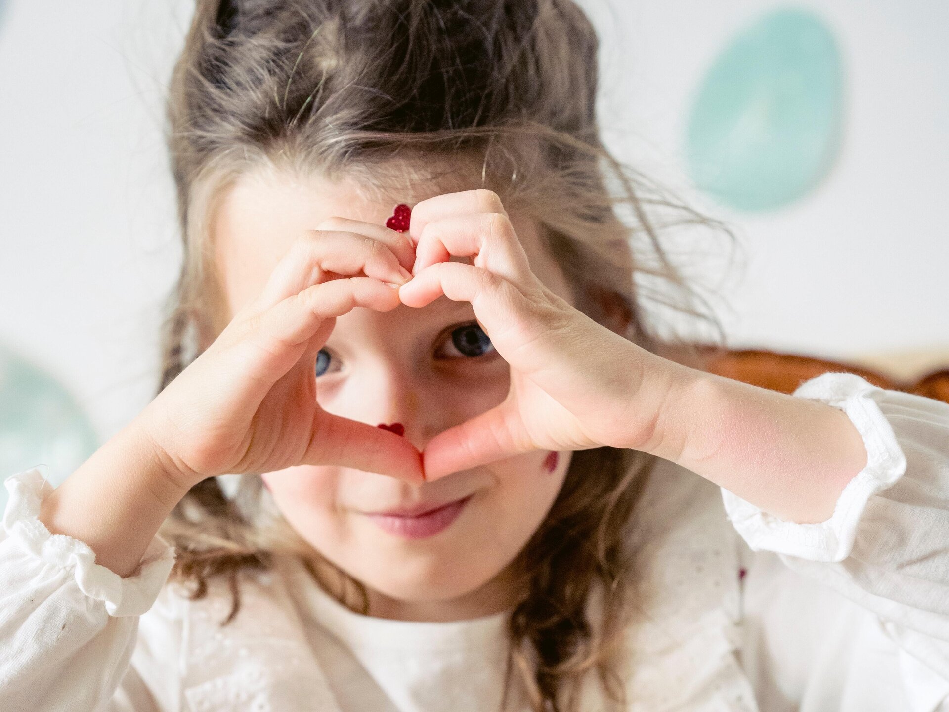 Zdjęcie przedstawia dziewczynkę, która wykonuje gest serca dłońmi. 