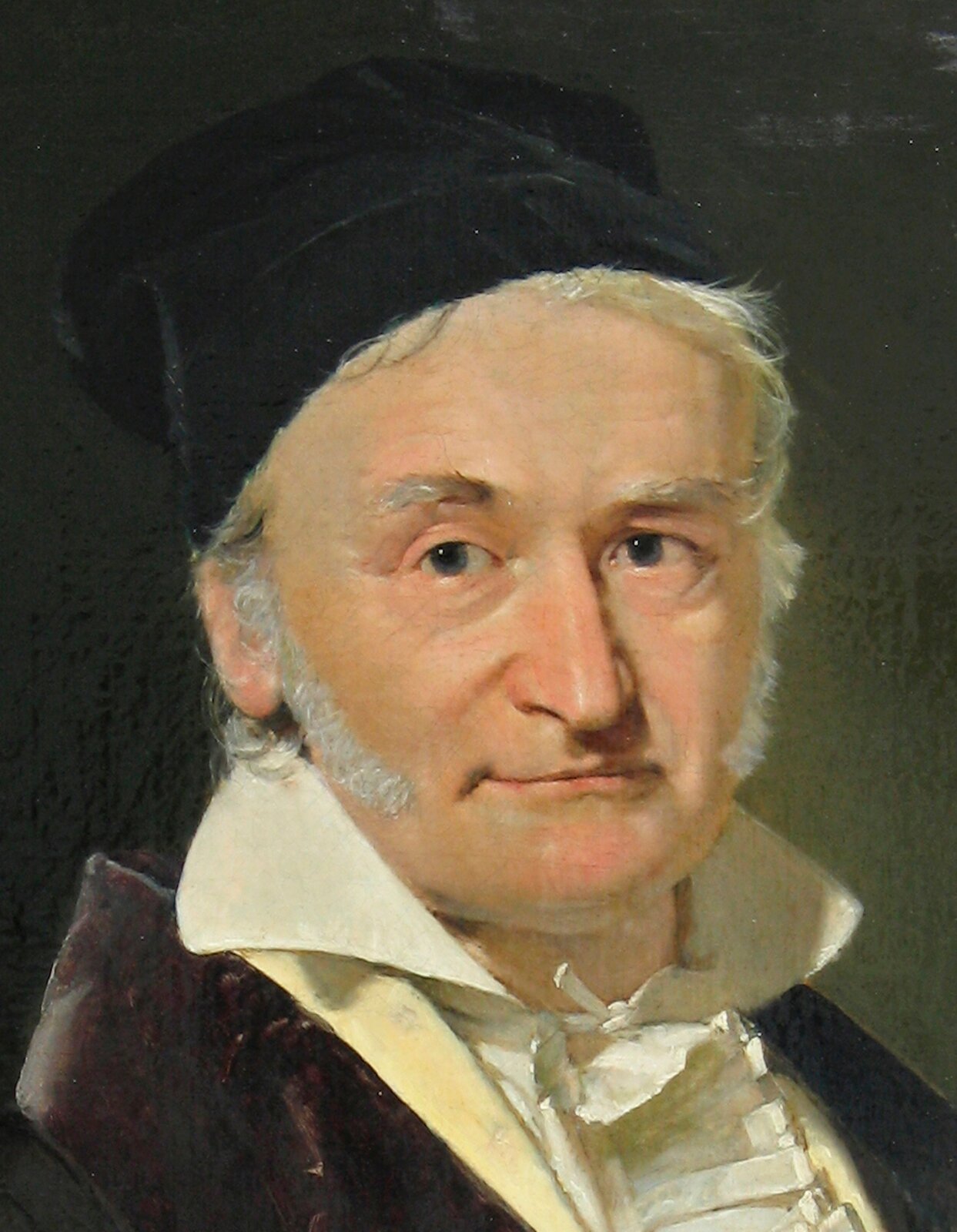 Rys. a. Rysunek przedstawia malowany farbami portret Carla Friedricha Gaussa. Jest to starszy mężczyzna o zaokrąglonej twarzy i wysokim czole. Ma długie bokobrody, które sięgają mu blisko ust. Mężczyzna lekko się uśmiecha. Na głowie ma założoną czarną czapkę. Nosi białą koszulę, zawiązaną pod szyją, z postawionym kołnierzem, a na koszuli brązowy surdut.