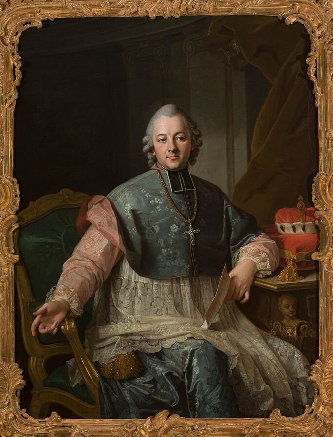 Ilustracja przedstawia portret mężczyzny w średnim wieku, siedzącego na fotelu. Jest ubrany w srebrzysto‑zieloną sutannę, na którą została nałożona koronkowa komża. Rękawy sutanny są jasnoróżowe. Na piersiach wisi krzyż na złotym łańcuchu. Na głowie ma siwą perukę ufryzowaną nad uszami w loki. Mężczyzna ma miłą twarz o wypielęgnowanej cerze, łagodne oczy, prosty nos i małe usta. W lewej ręce, opartej na stoliku trzyma kartkę papieru. Na stoliku leży czerwona poduszka, a na niej korona. W tle znajdują się dwie kolumny i atłasowa kotara.