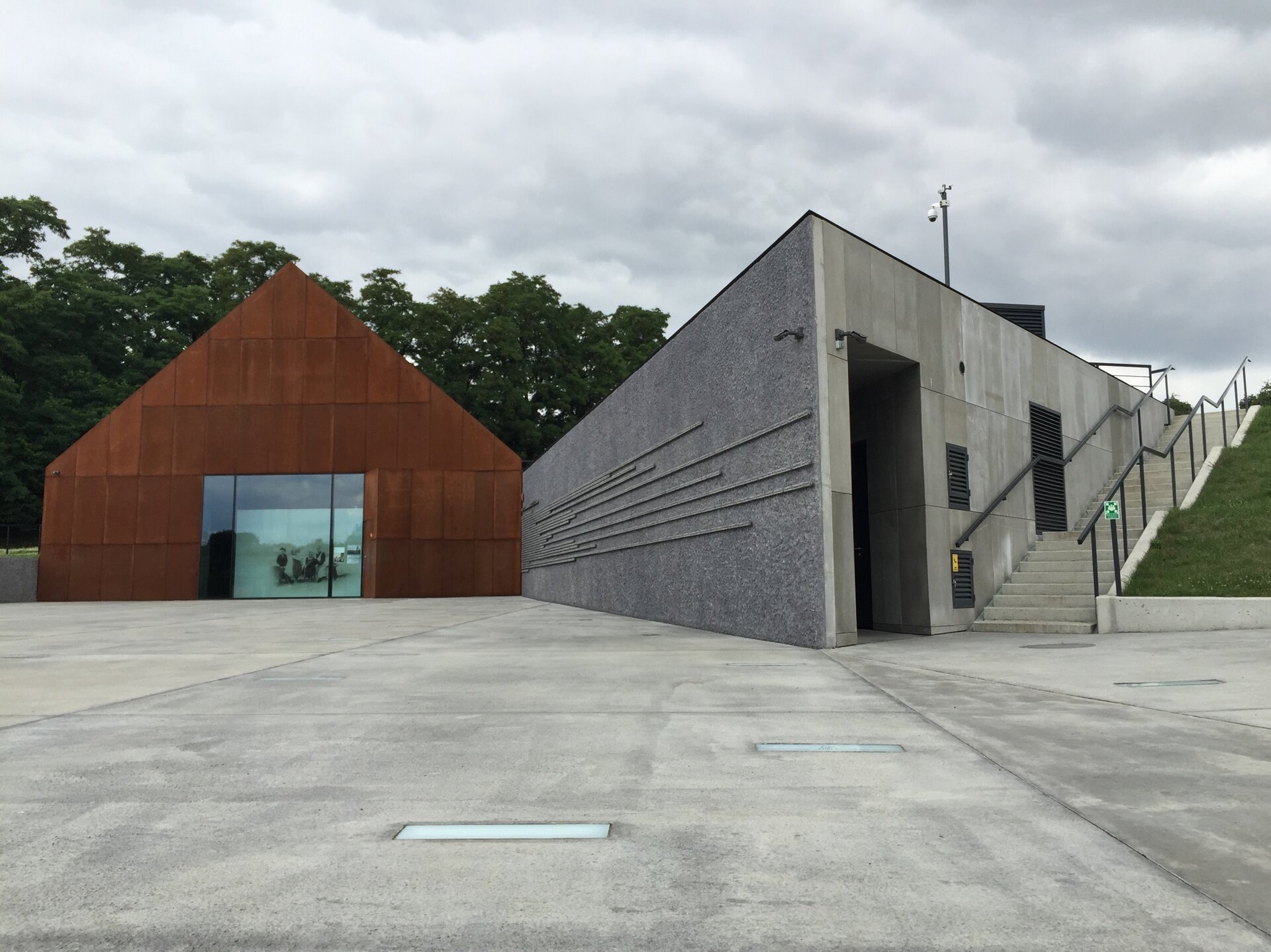 Zdjęcie przedstawia dziedziniec i dwa gmachy. Po prawej stronie znajdują się schodzące w dół na dziedziniec schody przy budynku w kształcie leżącego prostopadłościanu z oszczędną dekoracją naścienną. Po lewej stronie zdjęcia znajduje się widok budynku głównego muzeum w kształcie domu wiejskiego, którego fasada pokryta została imitacją rdzy. Na głównej fasadzie budynku jest szklana witryna ze zdjęciem rodziny Ulmów. Na placu muzealnym znajdują się nazwiska Polaków z regionu podkarpackiego, którzy za pomoc udzieloną Żydom w czasie Holokaustu zostali poddani represjom. W posadzce dziedzińca umieszczone są szklane tabliczki. 