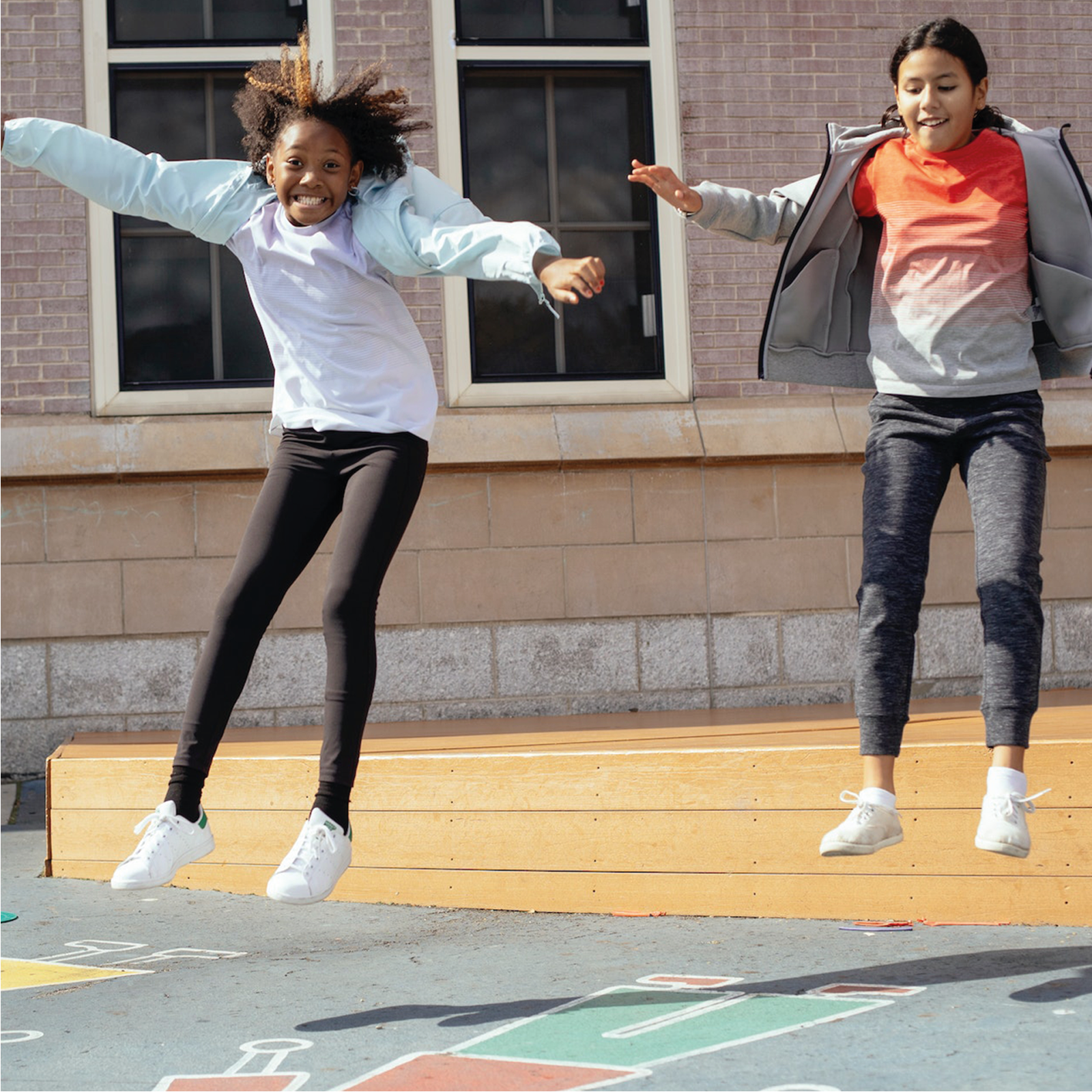 Zdjęcie ukazuje dwie dziewczynki w wieku szkolnym, które równocześnie podskakują bardzo wysoko w miejscu.