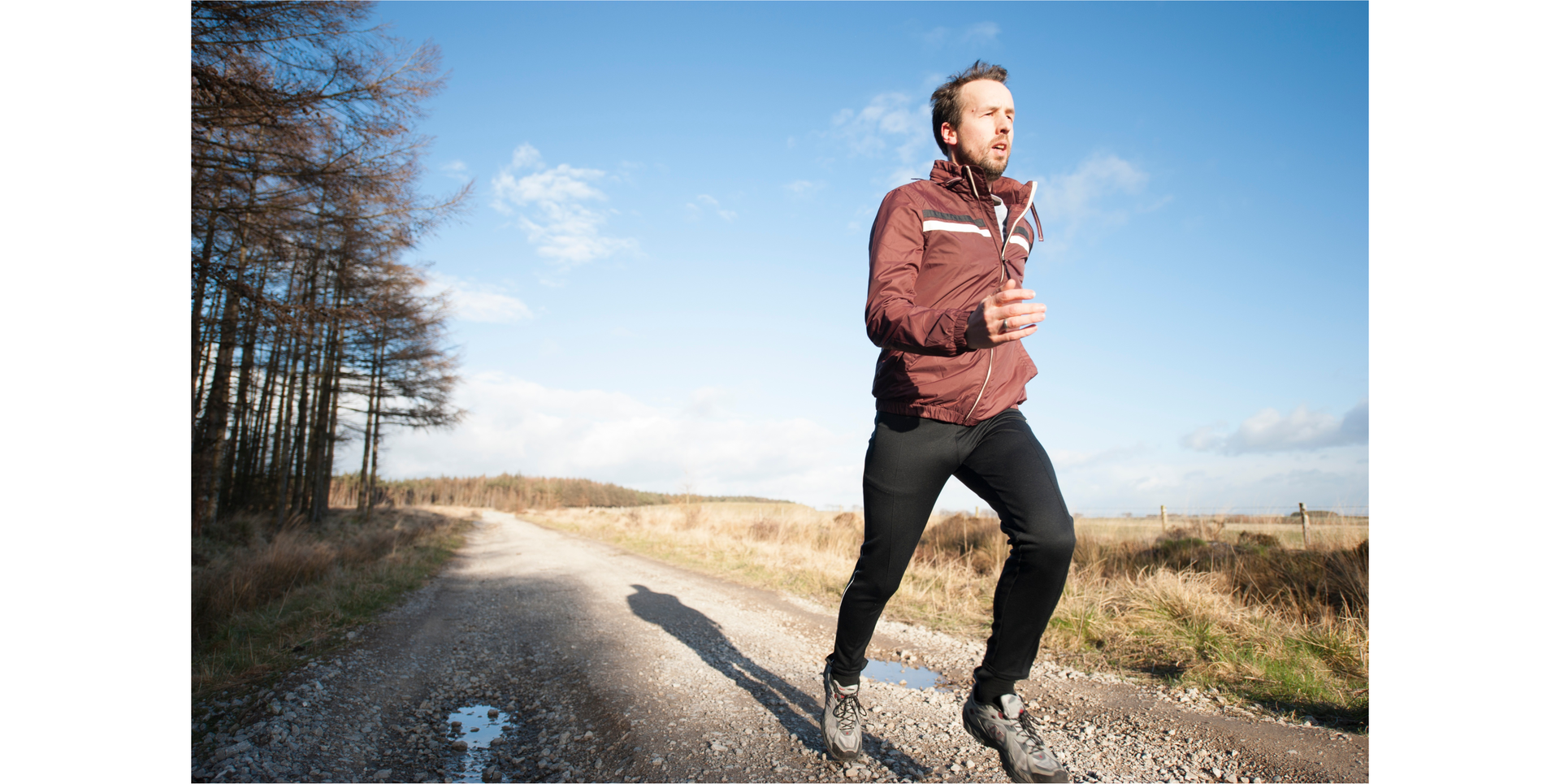 Zdjęcie przedstawia mężczyznę biegnącego polną drogą obok lasu. Mężczyzna ubrany jest w strój do biegania: sportowe buty, legginsy, lekką kurtkę. 