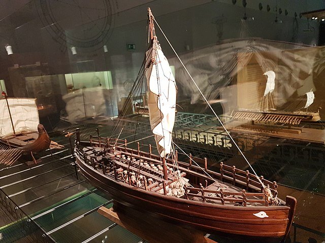 Zdjęcie przedstawia dużą łódź żaglową z jednym masztem i żaglem.