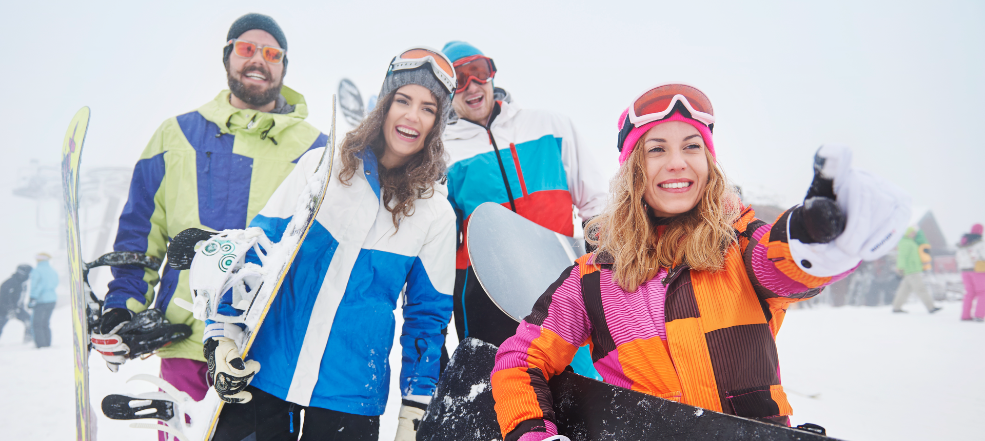 Zdjęcie przedstawia cztery młode osoby, które trzymają narty i deski snowboardowe. W tle stok.