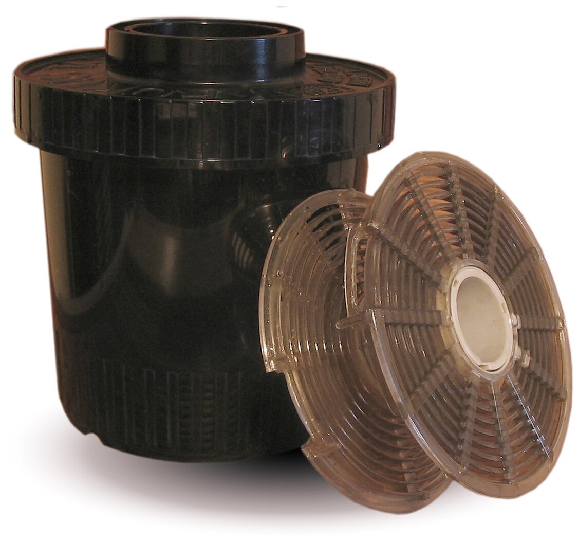 Zdjęcie przedstawia koreks. Widoczny jest cylindryczny pojemnik z nakładką u góry, której średnica jest większa niż pojemnika i w górnej części ma walcowatą wypustkę. Na prawo, oparty o pojemnik, widoczny jest szpulowaty przedmiot.