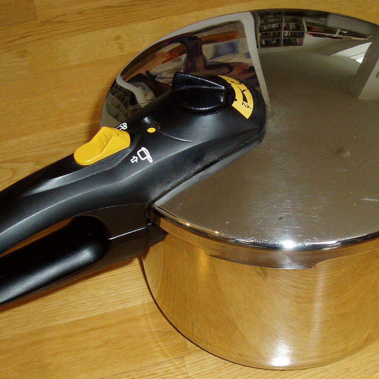 Zdjęcie przedstawia garnek z pokrywką zamykaną pod ciśnieniem. Widoczne pokrętło i żółty przycisk zamykający garnek.  Pod zdjęciem transkrypcja [odtwórz]