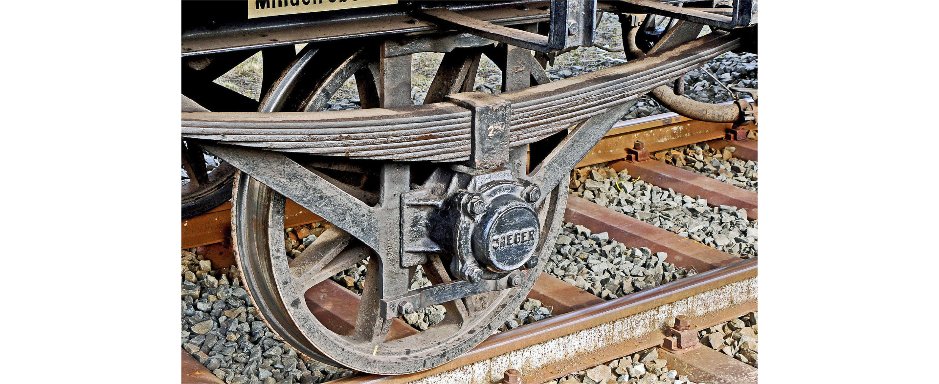 Zdjęcie przedstawia resory stalowe przy kołach starego wagonu stojącego na szynach.