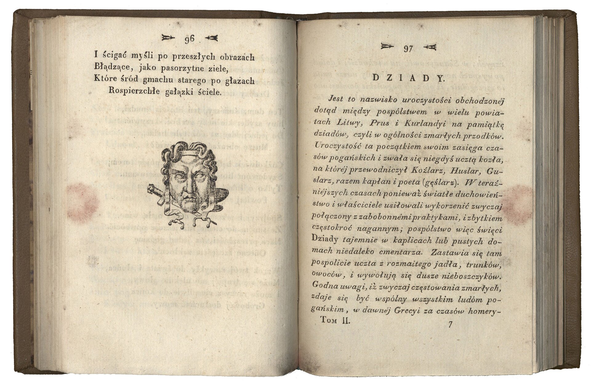 Fotografia otwartej książki. Z lewej strony wizerunek twarzy, maski, z prawej strony napis "Dziady" i tekst małą czcionką. Strona 96 i 97. Numeracja stron znajduje się w górnej części książki.