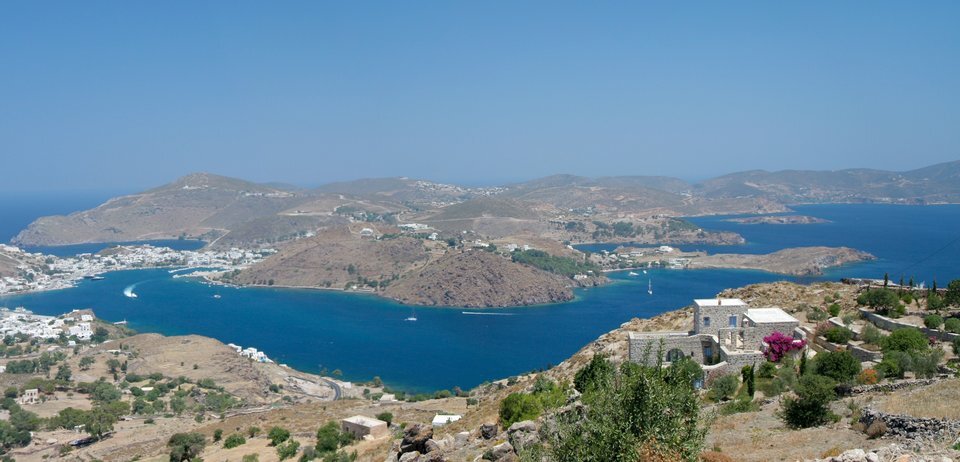 Zdjęcie przedstawia górzysty teren z nielicznymi, niewielkimi zabudowaniami oraz błękitne morze, na którym znajdują się niewielkie, skaliste wyspy.