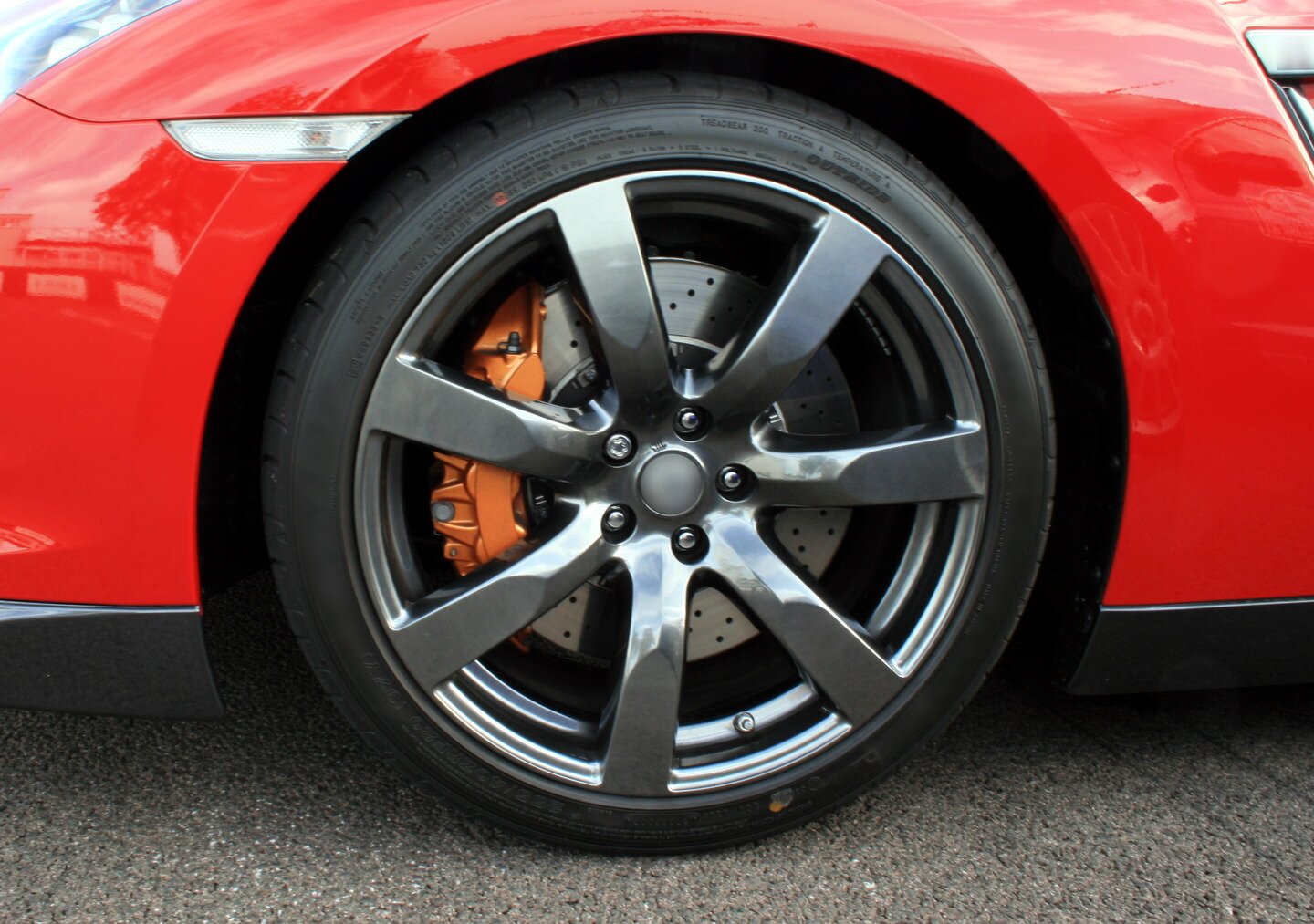 Ilustracja przedstawia fragment czerwonego samochodu- lewe przednie koło. 