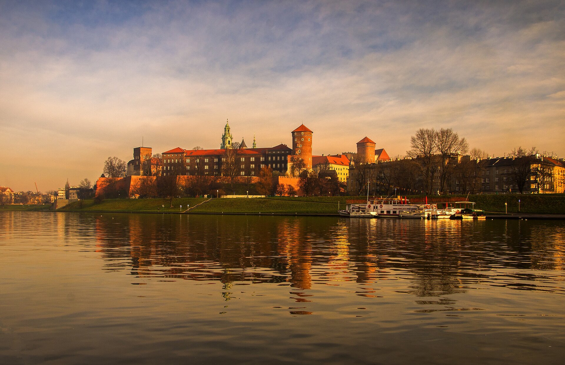 Fotografia przedstawia Wawel nad Wisłą w świetle zachodzącego słońca.