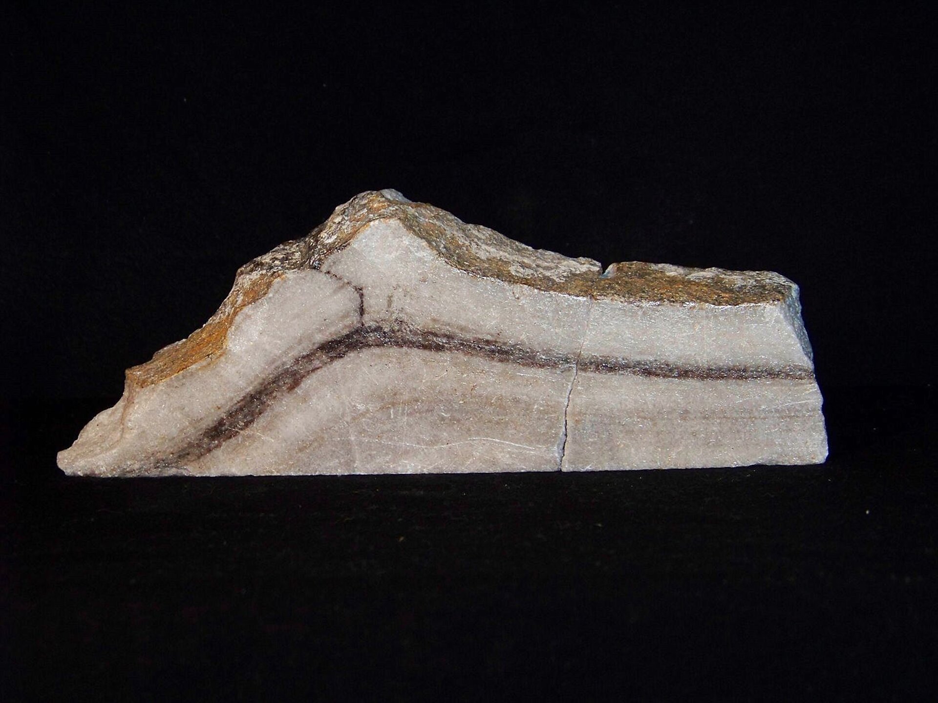 Fotografia przedstawia marmur o pociągłym, nieregularnym kształcie. Ma on beżowy kolor z ciemnym paskiem na środku oraz żółto‑białą wierzchnią stronę.