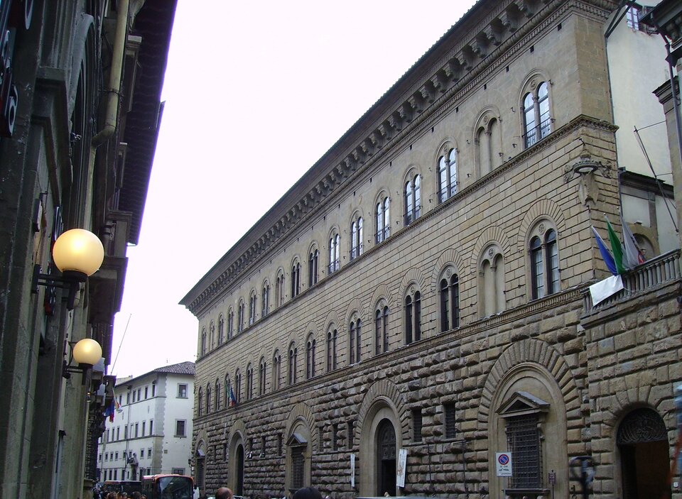 Fotografia przedstawia zabudowę miejską Florencji. Na pierwszym planie po prawej stronie ulicy znajduje się Pałac Medyceuszy. Jest to duża dwupiętrowa kamienica, z renesansowa kamienną fasadą w kolorze szarym. 