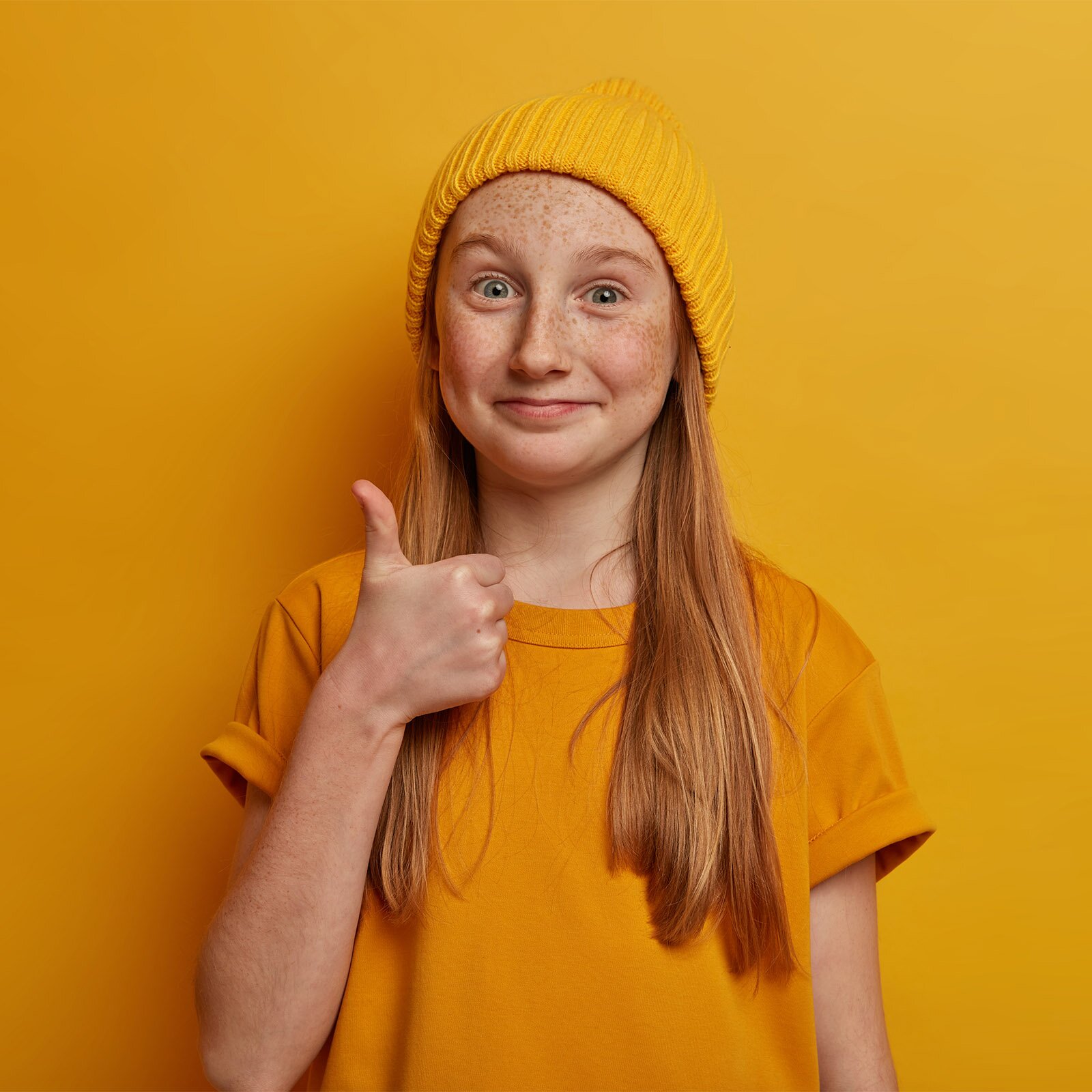 Zdjęcie przedstawia dziewczynkę w wieku około 11 lat, stojącą z uniesioną prawą ręką do góry. Jej dłoń jest złożona w pięść, podczas gdy kciuk jest wyprostowany ku górze. Takie ułożenie dłoni symbolizuje "OK".