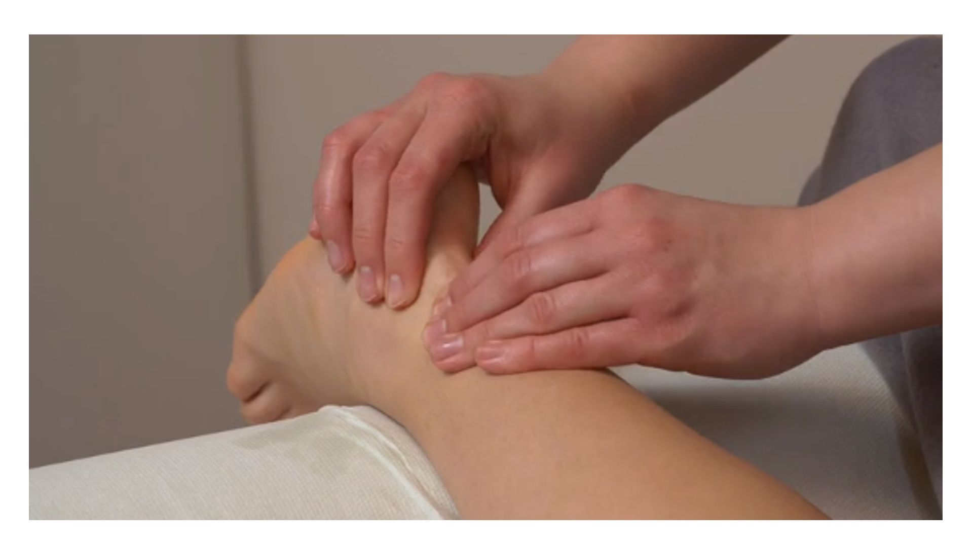 Zdjęcie pod tytułem przełamywanie ścięgna Achillesa. Zdjęcie przedstawia ręce masażystki uciskające przy użyciu opuszków palców okolicę kostki stopy pacjentki podpartej wałkiem.