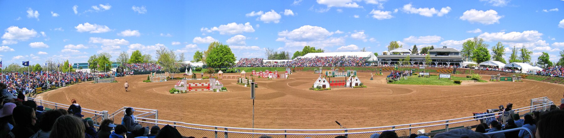 Na zdjęciu widoczny jest parkur. Składa się z
różnorodnych przeszkód ustawionych na torze. Są to między innymi konstrukcje służące do skakania przez drążki. Dookoła toru znajduje się publiczność.