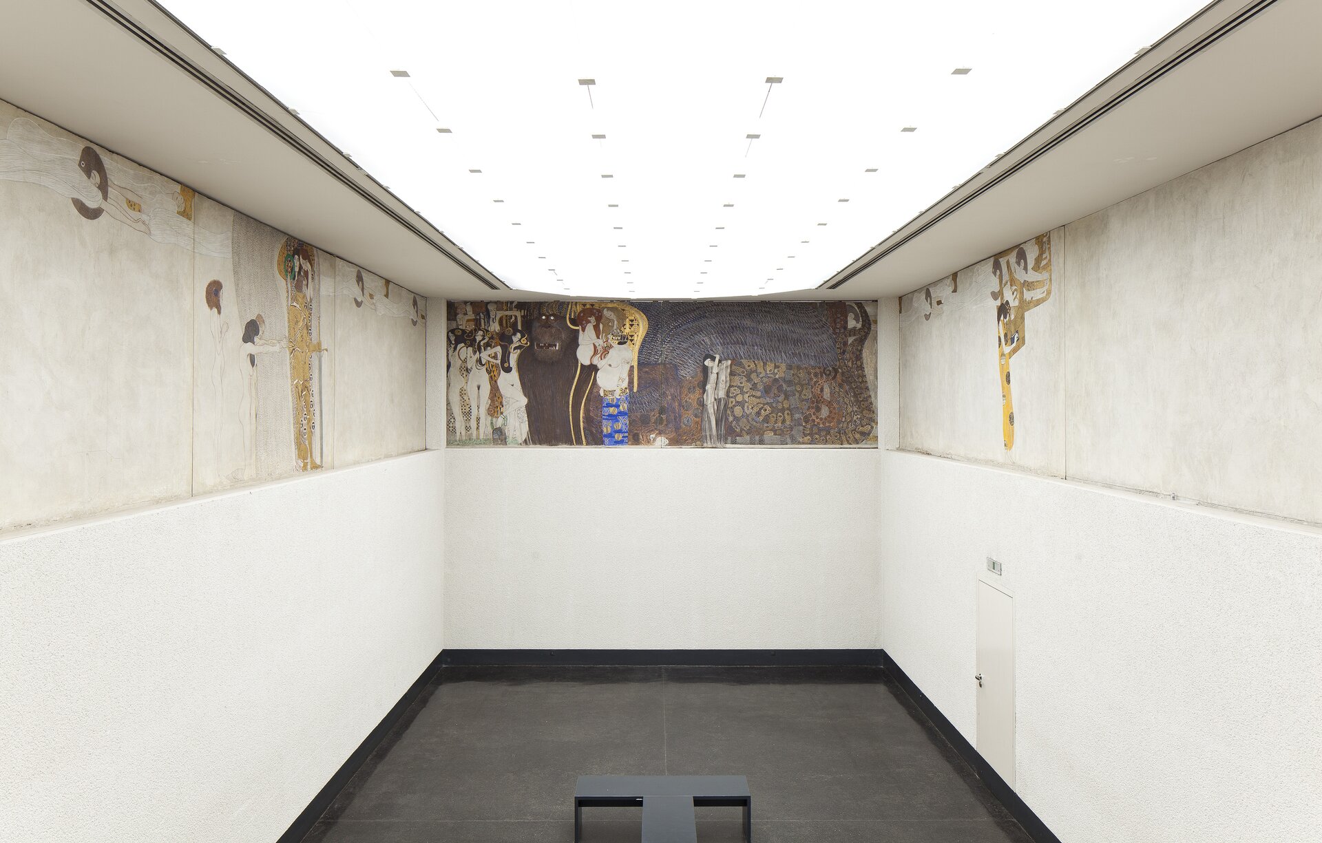 Ilustracja interaktywna o kształcie poziomego prostokąta przedstawia fresk „Fryz Beethovena”, znajdujący się w Pawilonie Secesji. Fresk ukazuje starożytne postacie stojące w różnych pozach. W kompozycji dominuje kolor biały. 