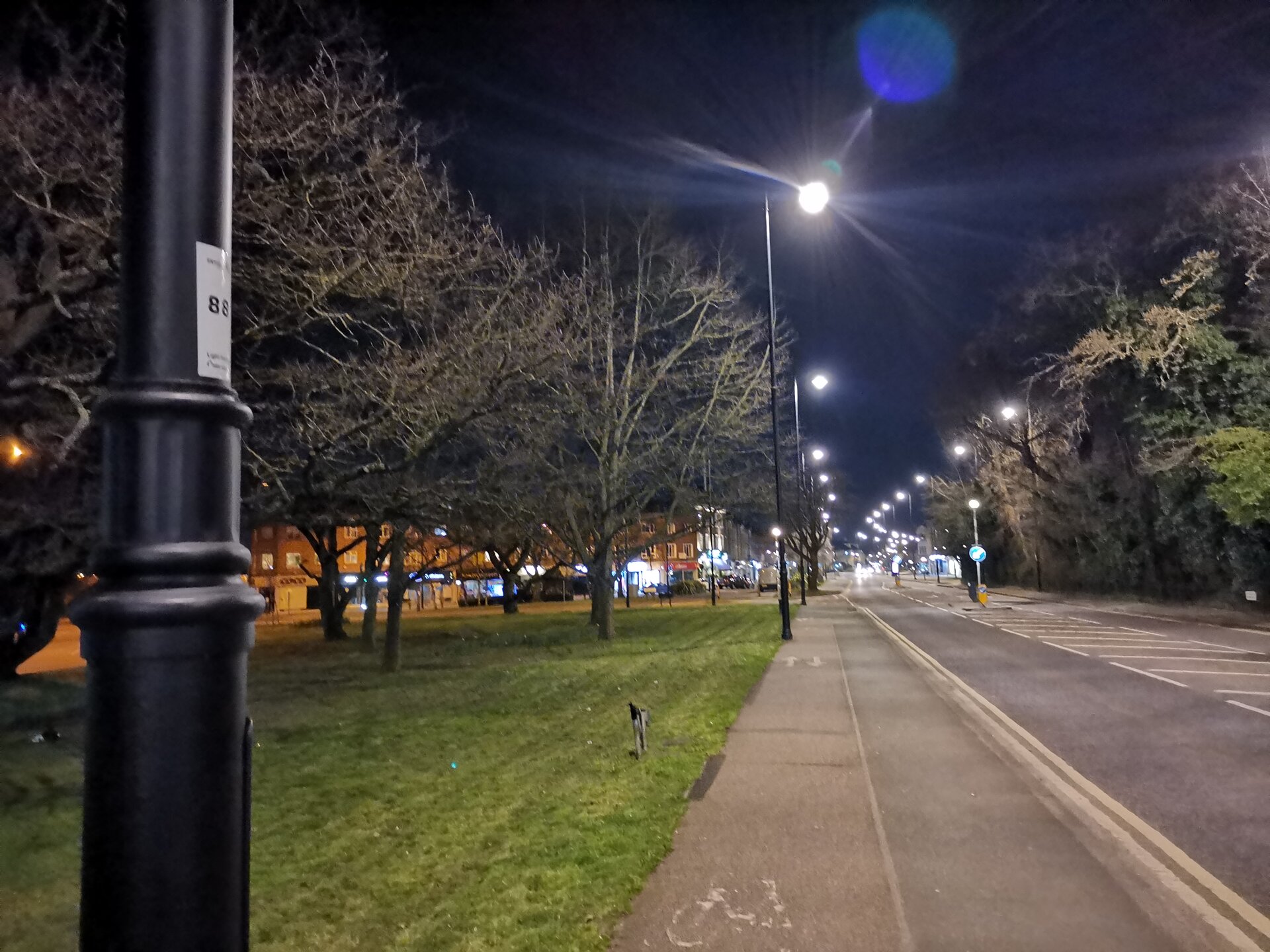 Zdjęcie przedstawia ulicę po zmroku w mieście. Wzdłuż ulicy stoją wysokie latarnie. Ich światło jest jasne.  