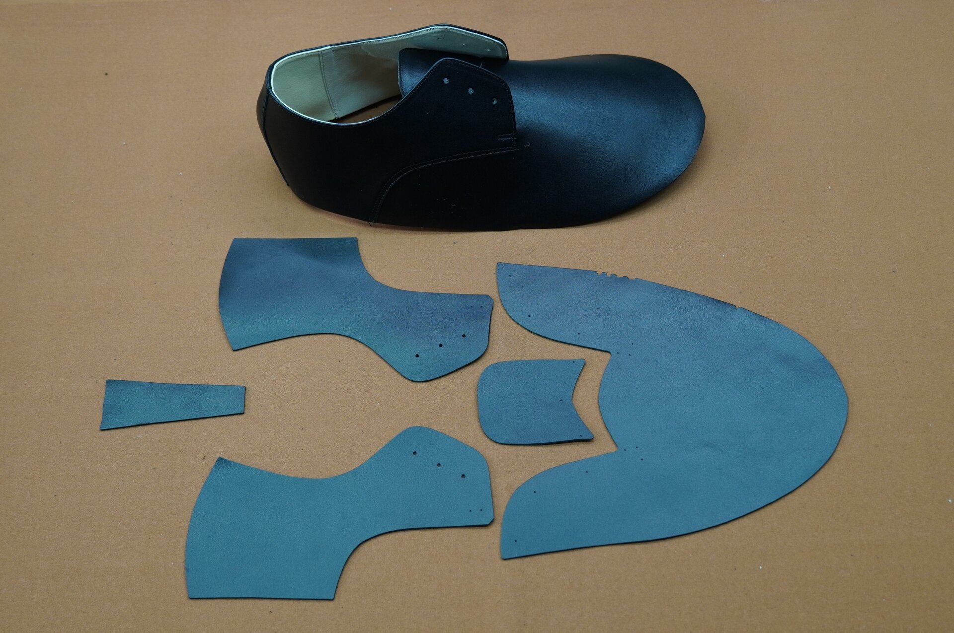 Zdjęcie przedstawia fragment cholewki uformowany w kształt buta i obok niego znajdujące się kawałki skóry w różnych kształtach, stanowiące elementy cholewki. Nagranie tożsame z treścią.