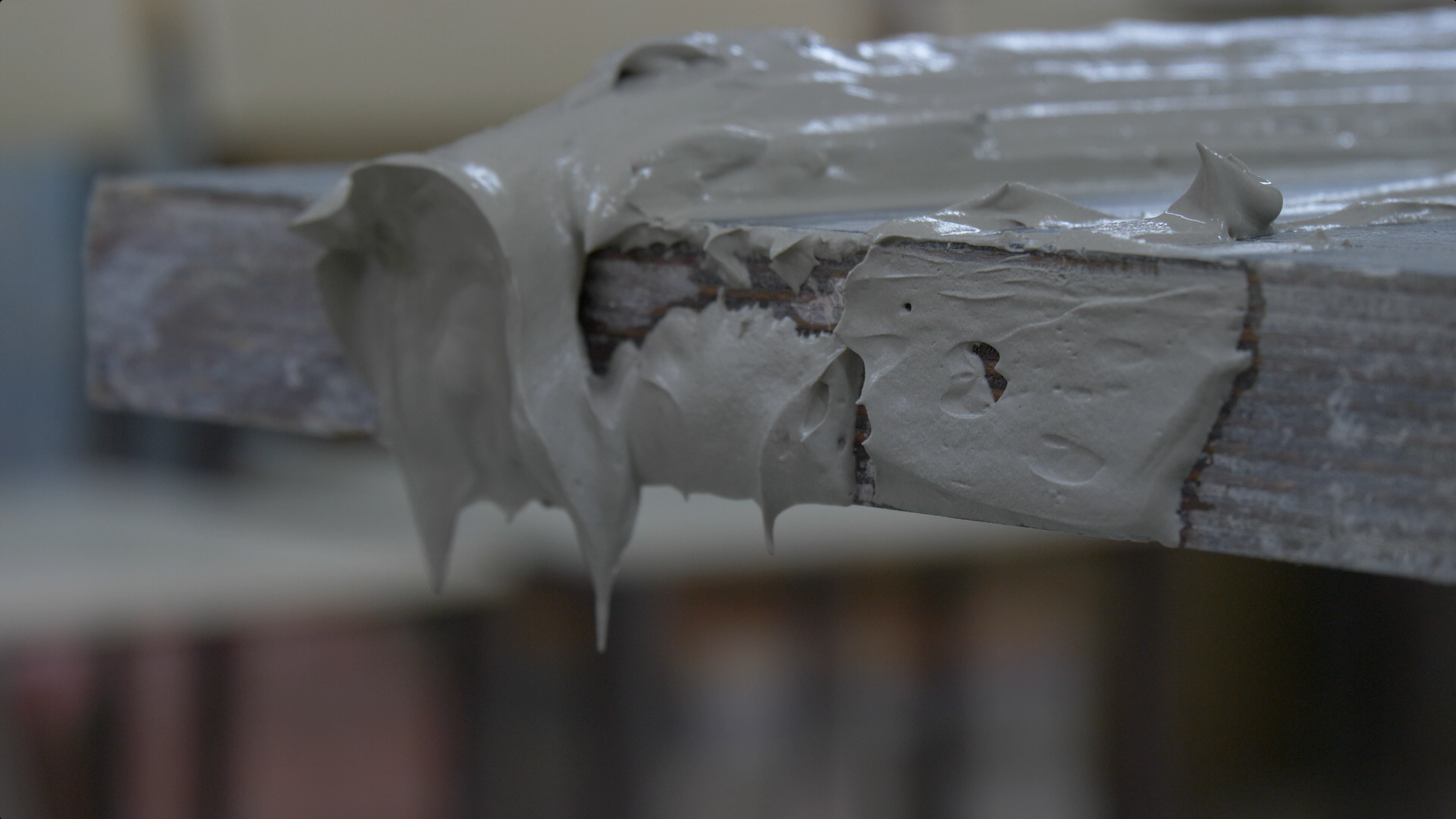 Zdjęcie przedstawia odlew elementu architektonicznego wykonany z zaprawy stiukowej. Zaprawa stiukowa w nieregularny sposób przylega do drewnianej powierzchni, tworząc element architektoniczny. 