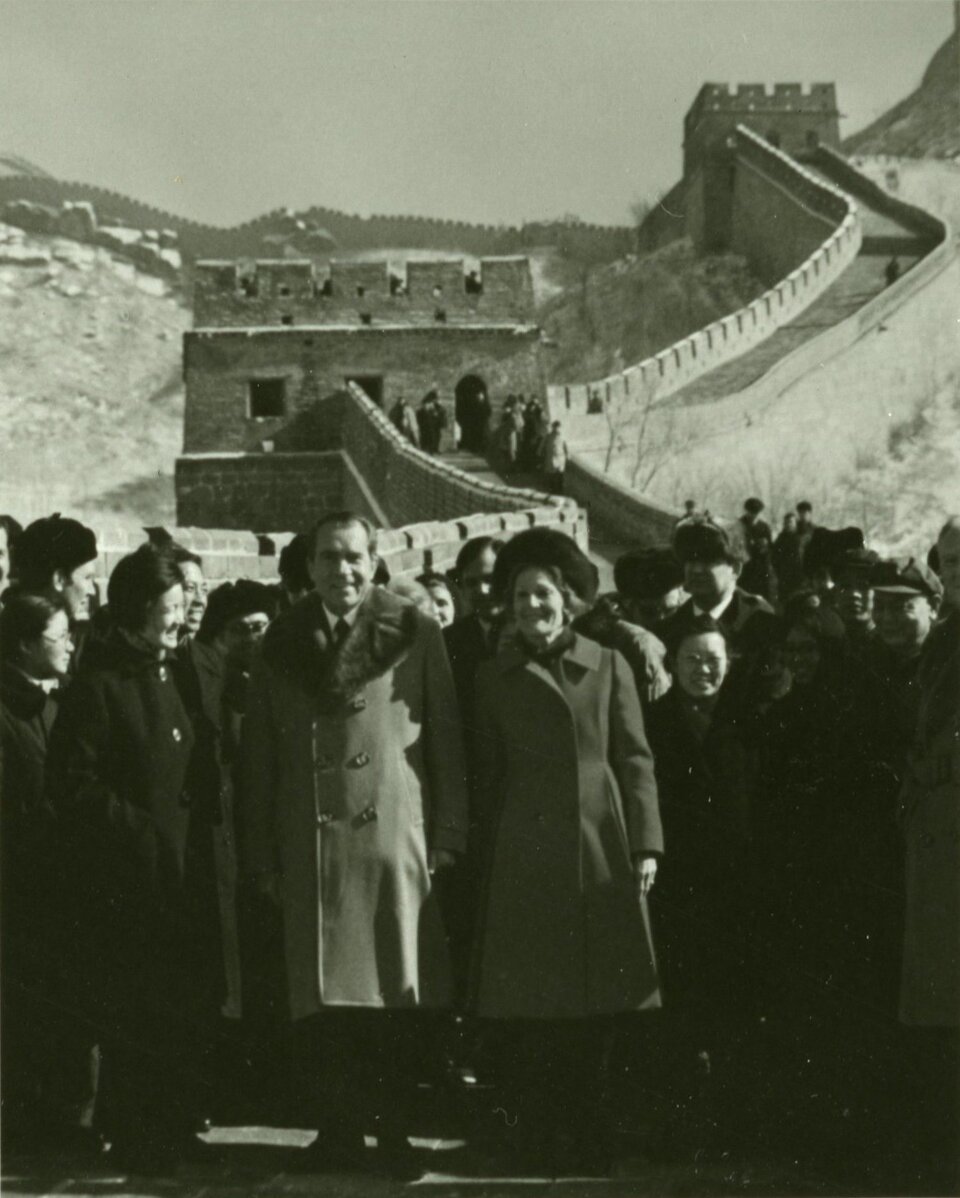 Zdjęcie przedstawia mężczyznę i kobietę w średnim wieku stojących pośród tłumu osób o azjatyckich rysach. Wszyscy zgromadzeni stoją na murze. Jest to Wielki Mur Chiński. 