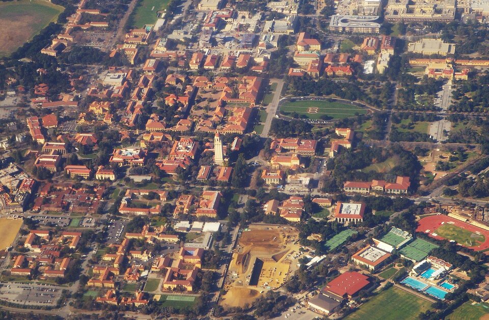Lotnicze zdjęcie kampusu Uniwersytetu Stanforda. Duża ilość niskich, najwyżej kilkupiętrowych budynków. Między nimi biegnie sieć dróg. Na terenie rozlokowane są również boiska i baseny.