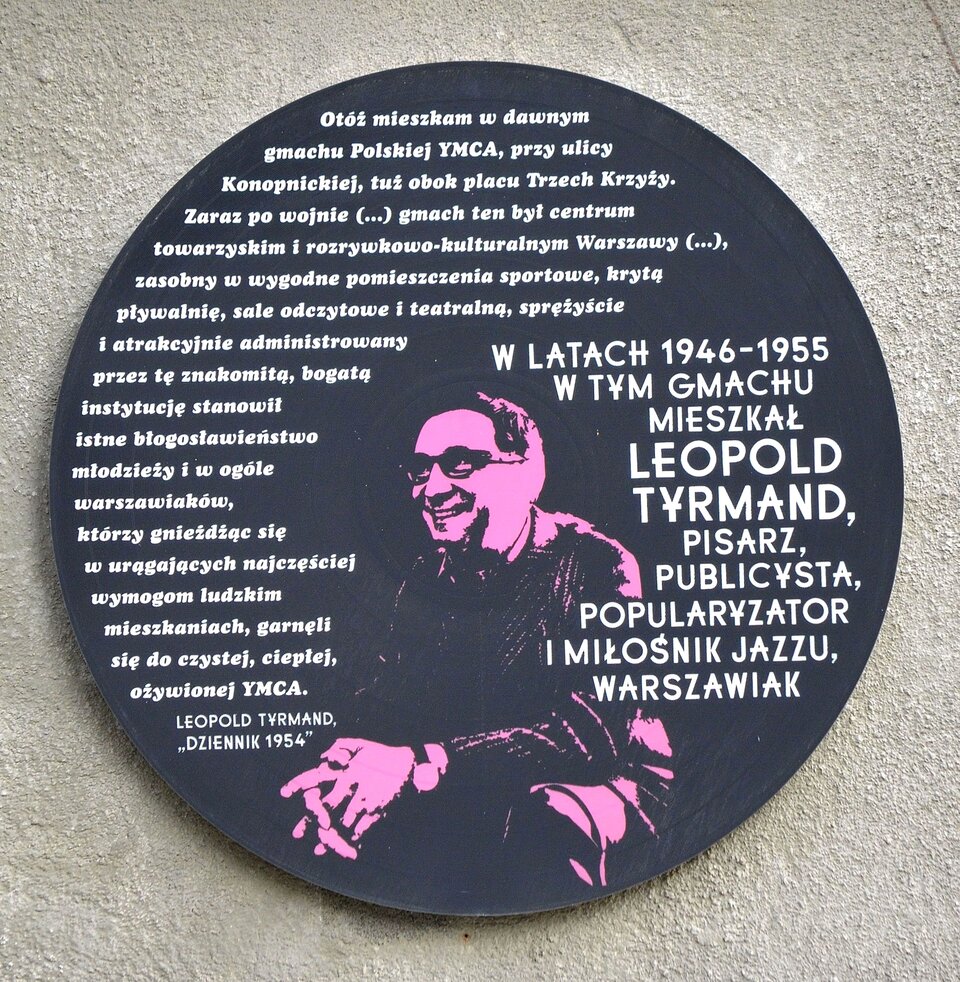 Tablica pamiątkowa Leopolda Tyrmanda w Warszawie. Na tablicy znajduje się zarys mężczyzny w średnim wieku. Mężczyzna jest uśmiechnięty, nosi okulary. Na tablicy w kształcie płyty gramofonowej poza podobizną Leopolda Tyrmanda i okolicznościowym tekstem znalazł się cytat z „Dziennika 1954”. Jest to wspomnienie pobytu pisarza w budynku YMCA o treści: „Otóż mieszkam w dawnym gmachu Polskiej YMCA, przy ulicy Konopnickiej, tuż obok placu Trzech Krzyży. Zaraz po wojnie (…) gmach ten był centrum towarzyskim i rozrywkowo‑kulturalnym Warszawy (…), zasobny w wygodne pomieszczenia sportowe, krytą pływalnię, sale odczytowe i teatralną, sprężyście i atrakcyjnie administrowany przez tę znakomitą, bogatą instytucję stanowił istne błogosławieństwo młodzieży i w ogóle warszawiaków, którzy gnieżdżąc się w urągających najczęściej wymogom ludzkim mieszkaniach, garnęli się do czystej, ciepłej, ożywionej YMCA".
