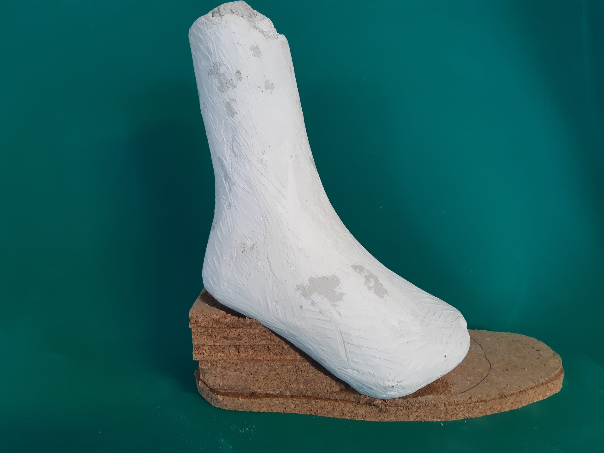 Zdjęcie przedstawia odlew gipsowy stopy oraz warstwy płyt suberytowych, przygotowanych do wstępnego dopasowania do odlewu.