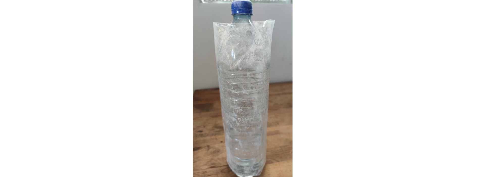 Zdjęcie 5. Zgrzany i wytalkowany rękaw foliowy naciągnięty na plastikową butelkę o pojemności 1,5 l, wypełnioną wodą.