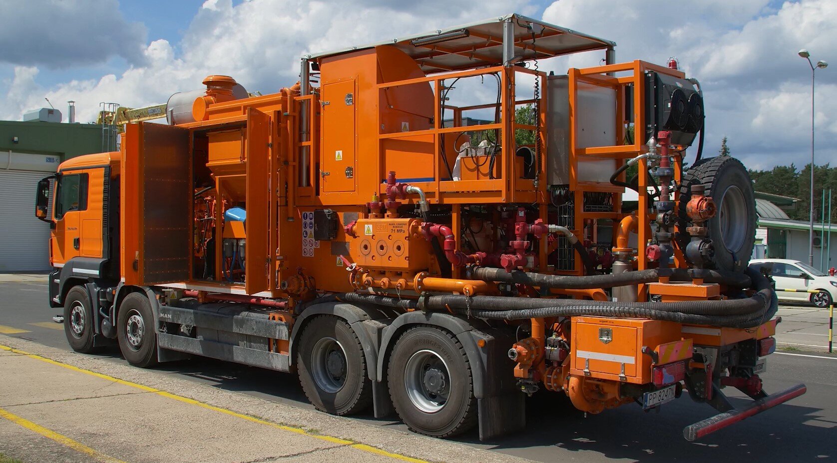 Na zdjęciu widać agregat cementacyjny na podwoziu samochodowym widzianym pod kątem.Agregat osadzony jest na podwoziu samochodowym, które ma cztery koła po każdej ze stron. Pomiędzy kabiną kierowcy a tylną częścią podwozia znajduje się element o kształcie pomarańczowego prostopadłościanu z zamykanymi drzwiami. Jest to szafla w której widoczne są elementy do agregatu. W tylnej części podwozia znajduje się platforma zabezpieczona barierką ochronną. Poniżej biegną rury łączą się z prostopadłościennym elementem będącym pompą. Rury i węże są połączone ze sobą. Z tyłu podwozia samochodowego jest podwieszone koło zapasowe.