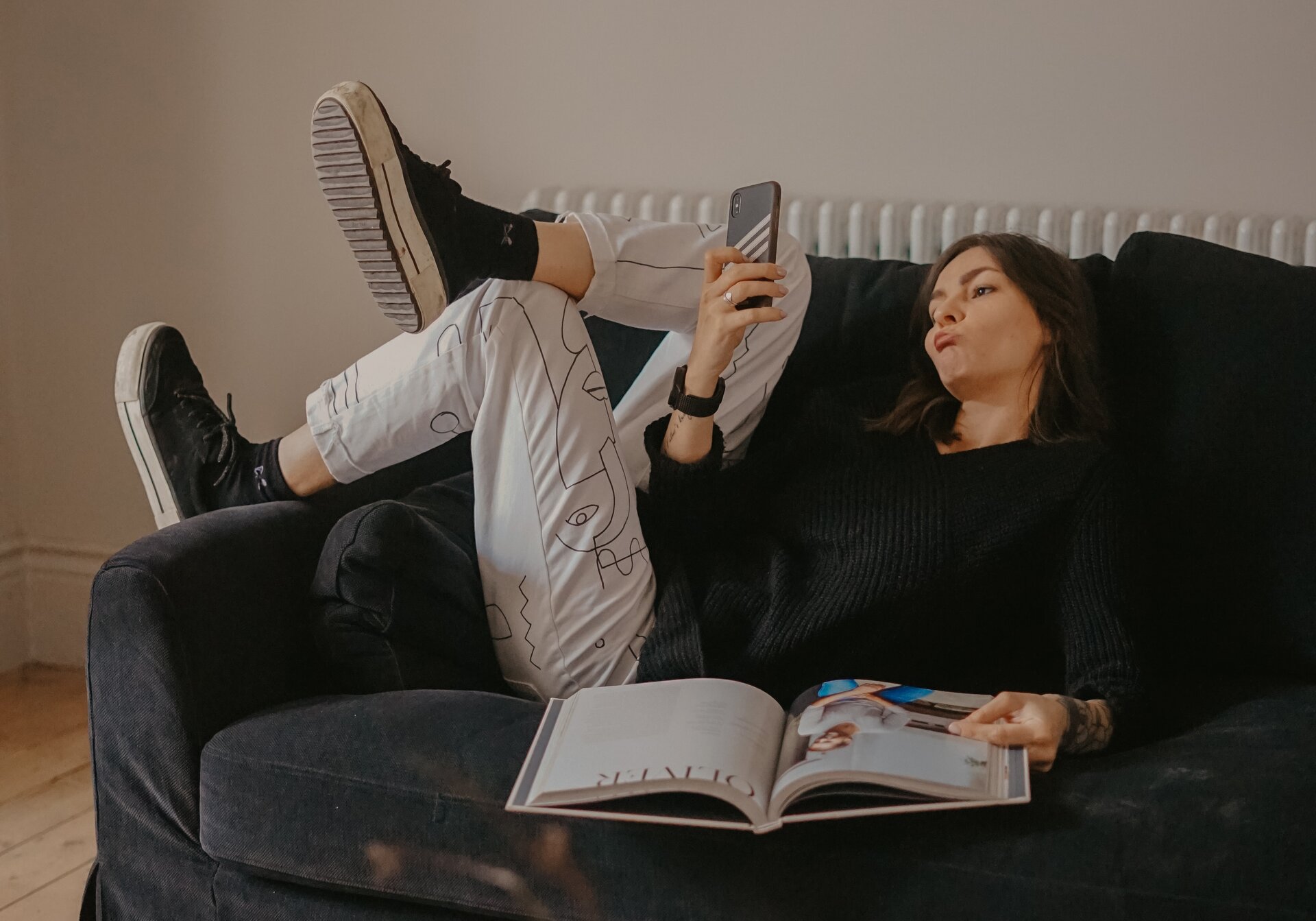 Zdjęcie przedstawia nastolatkę odpoczywającą na kanapie z telefonem w ręku, w który jest wpatrzona. 