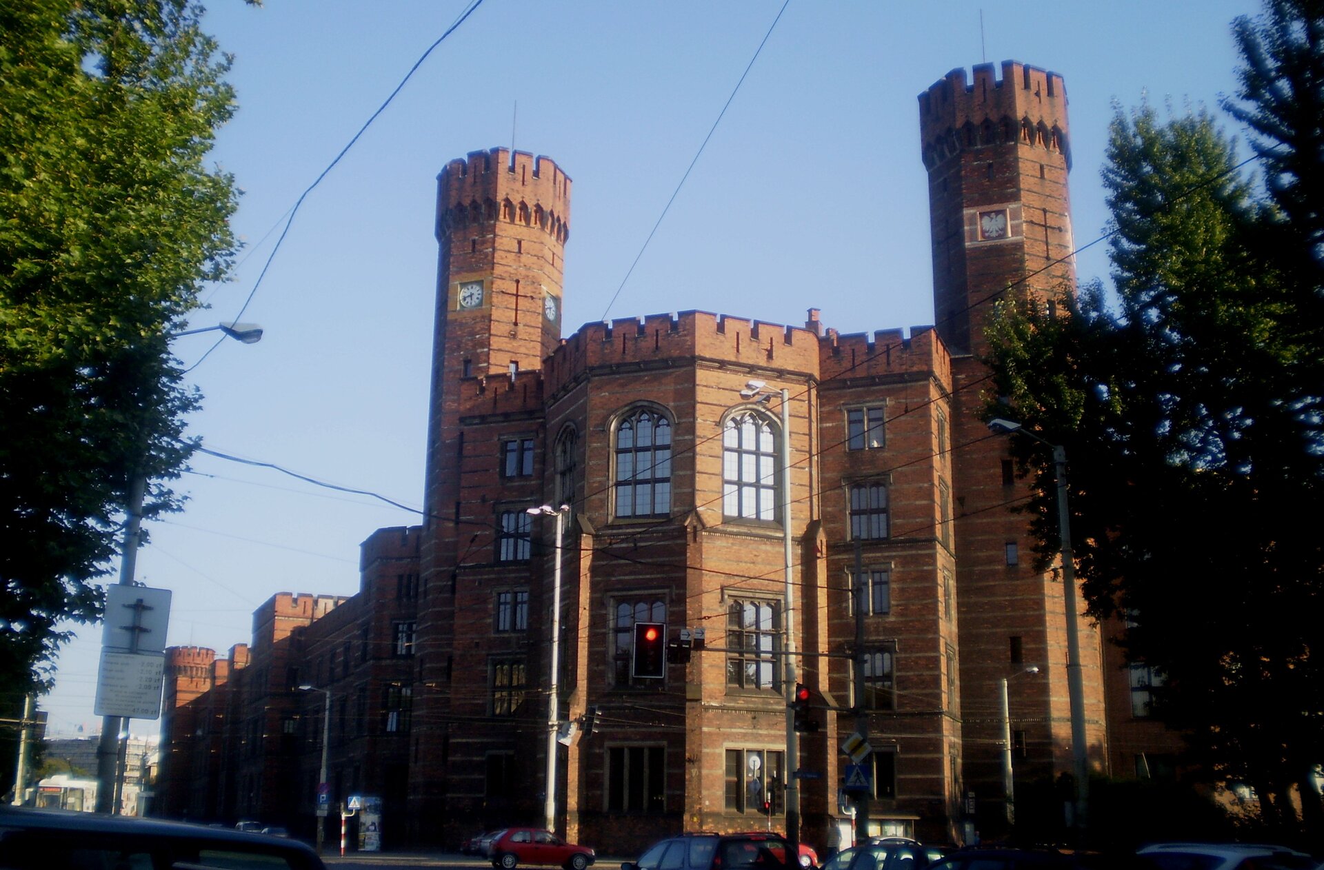 Kliknij żeby powiększyć Zdjęcie, które przedstawia Sąd Okręgowy we Wrocławiu. Przypomina gotycki zamek z dwiema wieżami, zbudowany z czerwonej cegły. Na wieżach sądu umieszczono zegar i godło państwa polskiego. Gmach został ozdobiony piaskowymi gzymsami.