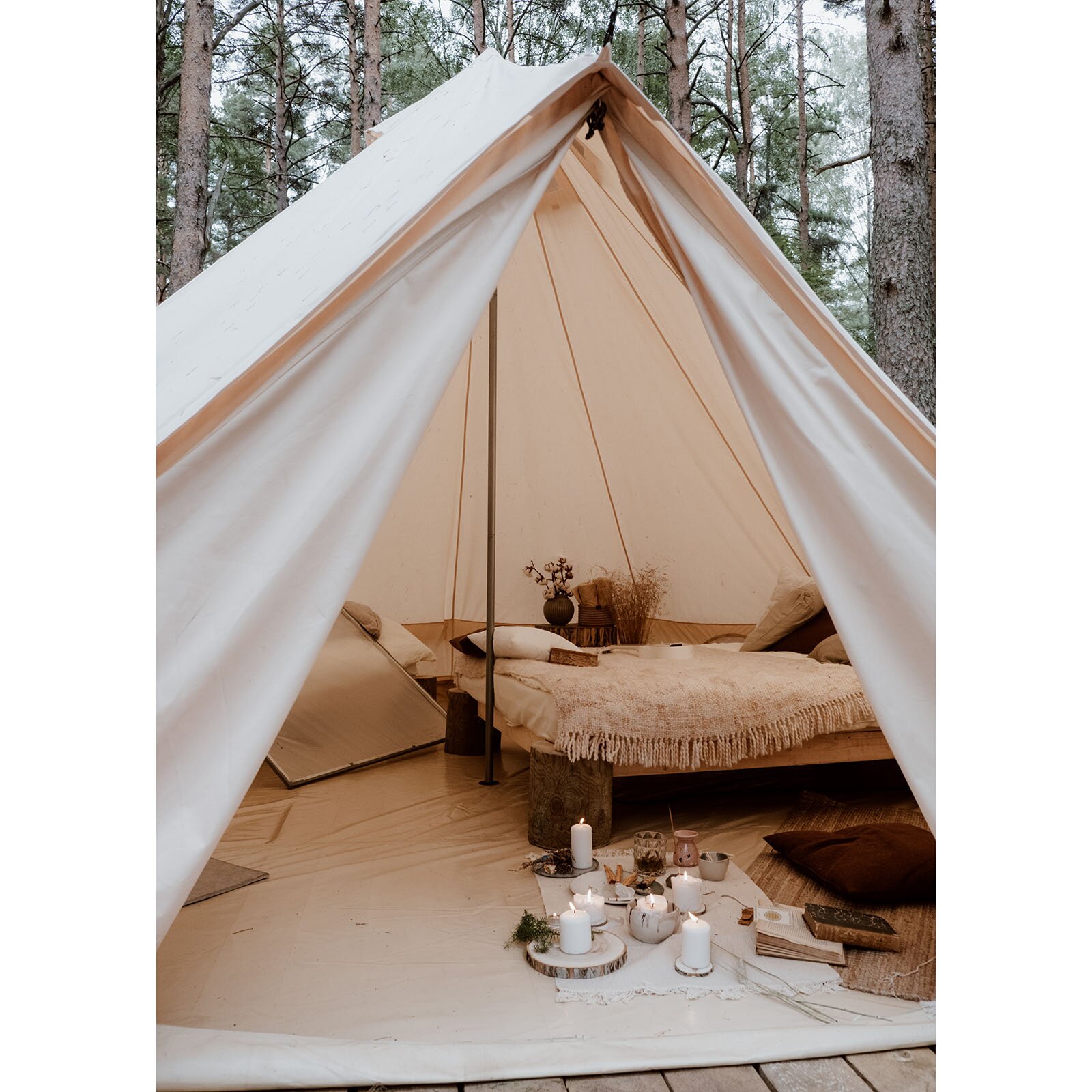 Zdjęcie przedstawia wnętrze namiotu, w którym ustawiono drewniane łóżko zakryte narzutą z frędzlami. Na podłodze ustawiono kilka zapalonych świec. Koło łóżka postawiono wazony z kwiatami. 