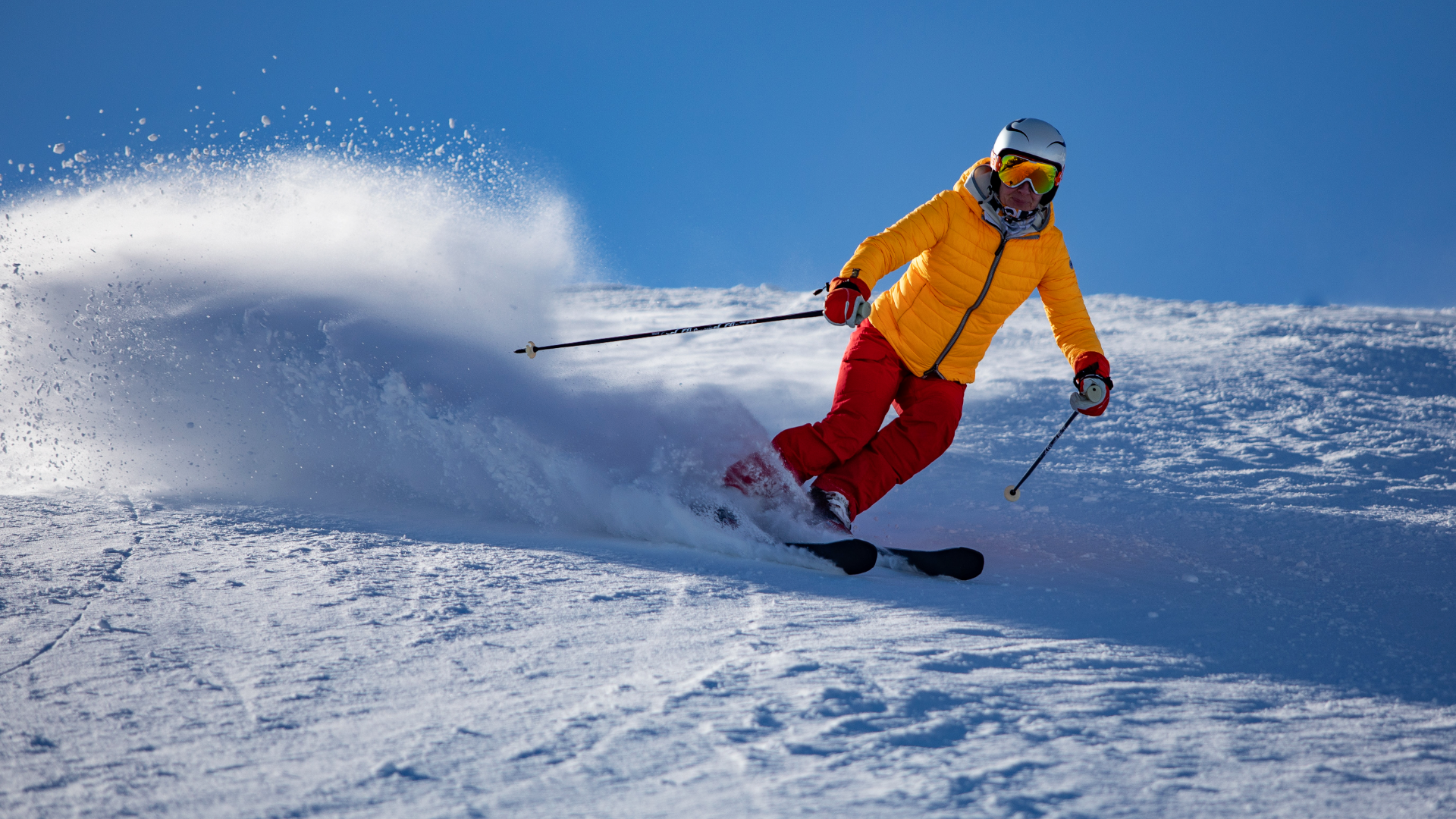 Zdjęcie przedstawia osobę zjeżdżającą na nartach. Osoba ubrania jest w strój narciarski, ma kask i gogle.