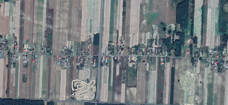 Zdjęcie przedstawia widok z góry na płaski teren. Przy ulicy biegnącej przez teren stoją zabudowania.    