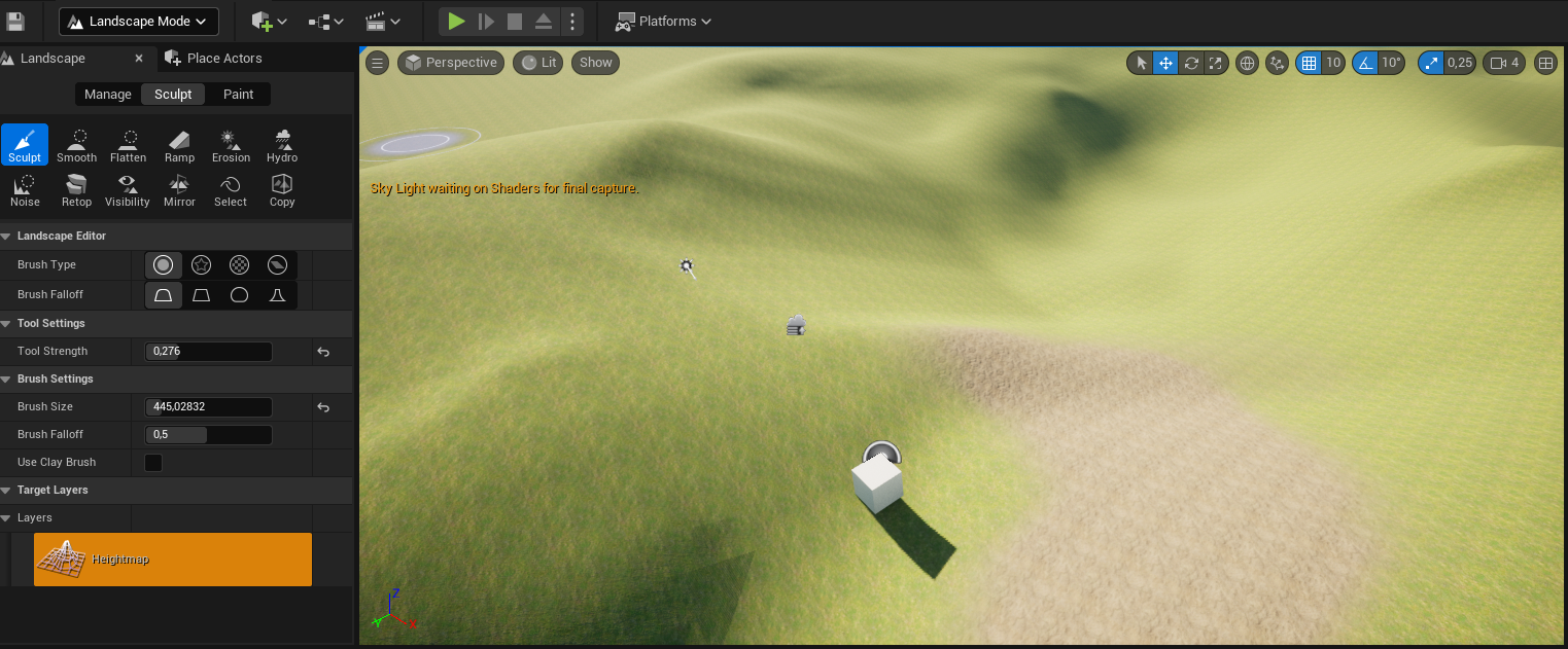 Ilustracja przedstawia zrzut ekranu - panel programu  Unreal Engine . Widoczny jest ekran z rozległą płaszczyzną z licznymi wgłębieniami i wybrzuszeniami w kolorze zielono - beżowym. Bliżej dolnej krawędzi znajduje się mały, biały sześcian, z cieniem biegnącym w skośnie w stroną dołu ekranu, a za nim szary punkt, a dalej symbol różdżki. W lewym górnym rogu widać szare koło obwiedziony konturami okręgów o większej średnicy. Pod okręgiem widoczny jest napis:  Sky Light waiting on Shaders for final capture . Na górze ilustracji znajdują się ułożone w rzędzie symbole graficzne, a lewej strony lista menu z następującymi opcjami: okienko z wybraną opcją:   Landscape Mode , dwie zakładki:  Landscape  i  Place Actors , trzy opcje z wybraną opcją środkową:  Manage, Sculpt, Paint , a pod spodem dwa szeregi ikonek z podpisami. Wybrana jest pierwsza ikonka w górnym rzędzie z symbolem dłuta i podpisem  Sculpt . Poniżej, w kolejnych linijkach znajdują się grupy opcji menu: pierwsza z nich to  Landscape Editor  z opcjami:  Brush Type:  - wybrana jest tu ikonka koła obwiedzionego okręgiem większej średnicy oraz  Brush Falloff  z wybraną ikonką przypominającą trapez z zaokrąglonymi górnymi rogami; druga z nich to:  Tool Settings  z opcją:  Tool Strength:  i wpisaną wartością 0,276; trzecia grupa opcji menu to:  Brush Settings  z opcją:  Brush Size  i wpisaną wartością 445,02832,  Brush Falloff  i wpisaną wartością 0,5 i odznaczoną opcją:  Use Clay Brush ; czwarta grupa opcji menu to:  Target Layers , a piąta  Layers  z pomarańczowym przyciskiem z ikonką siatki terenu z widocznym wybrzuszeniem oraz napisem:  Heightmap . 