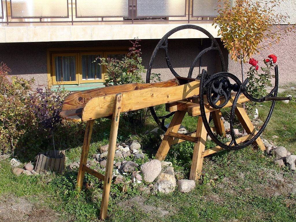 Na zdjęciu widzimy drewnianą maszynę rolniczą z dużym metalowym kołem służącą do cięcia zboża i roślin pastewnych na drobne kawałki.