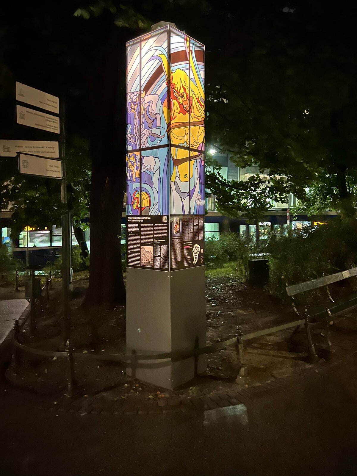 Zdjęcie wykonane w nocy przedstawia podświetloną kolumnę, która składa się z dwóch części – dolnej oraz górnej. Dolna część to dwukolorowy (szary u dołu i czarny u góry) prostopadłościan na którym umieszczono plansze informacyjne o wydarzeniu. Górna część kolumny to ekrany na których wyświetlane są witraże. Na ekranach wyświetlono witraż przedstawiający tors młodego mężczyzny. Postać ta ma długie włosy i spogląda na ziemię. Obok, z lewej strony stoją bliżej nieokreślone zdeformowane postaci. Witraże mają jaskrawe kolory. Tło fotografii stanowi rozświetlony budynek.